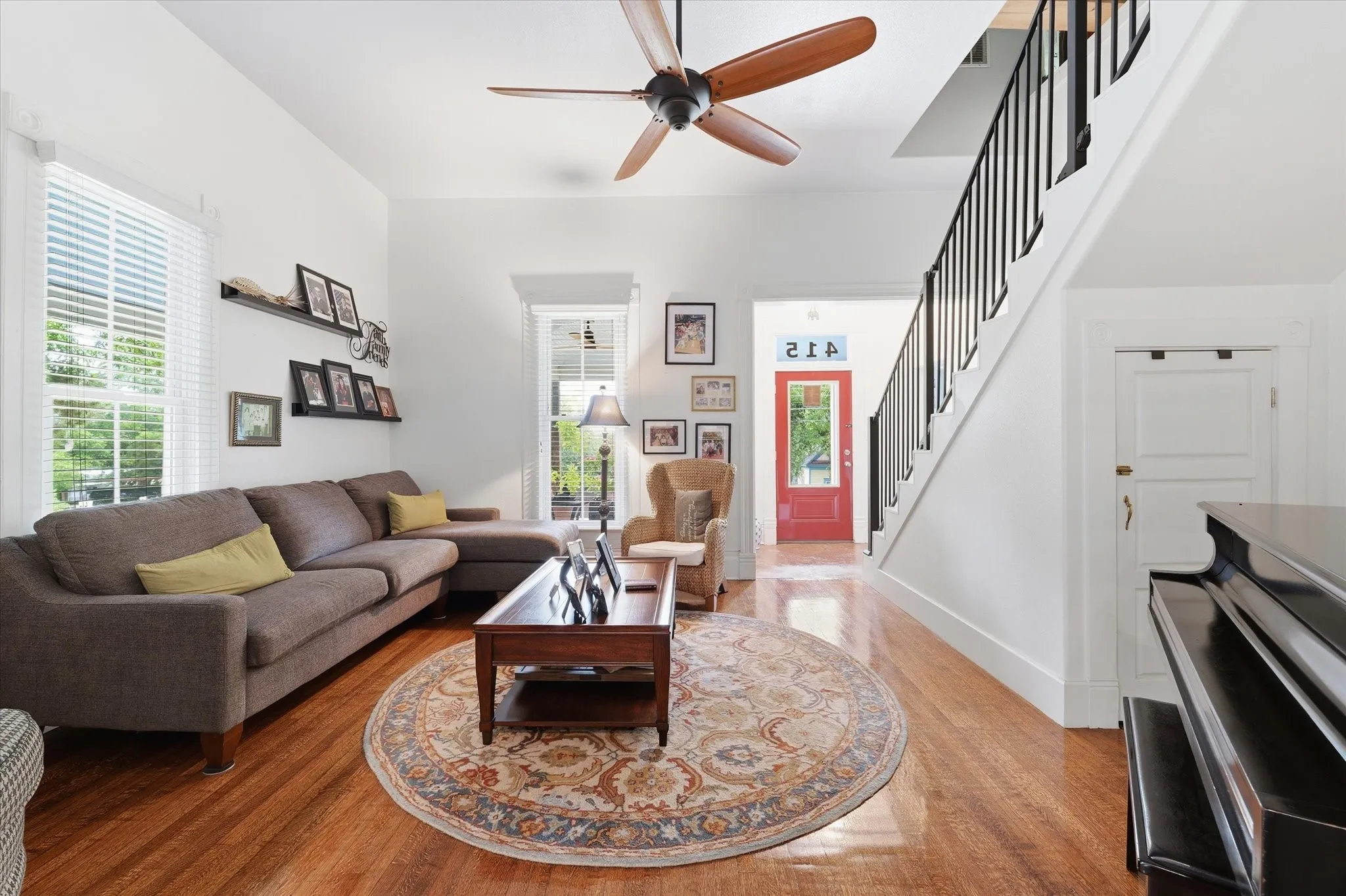 Oak hardwood flooring extending throughout the living space, 12' ceilings, a large ceiling fan, white trim, and a staircase with black metal balusters