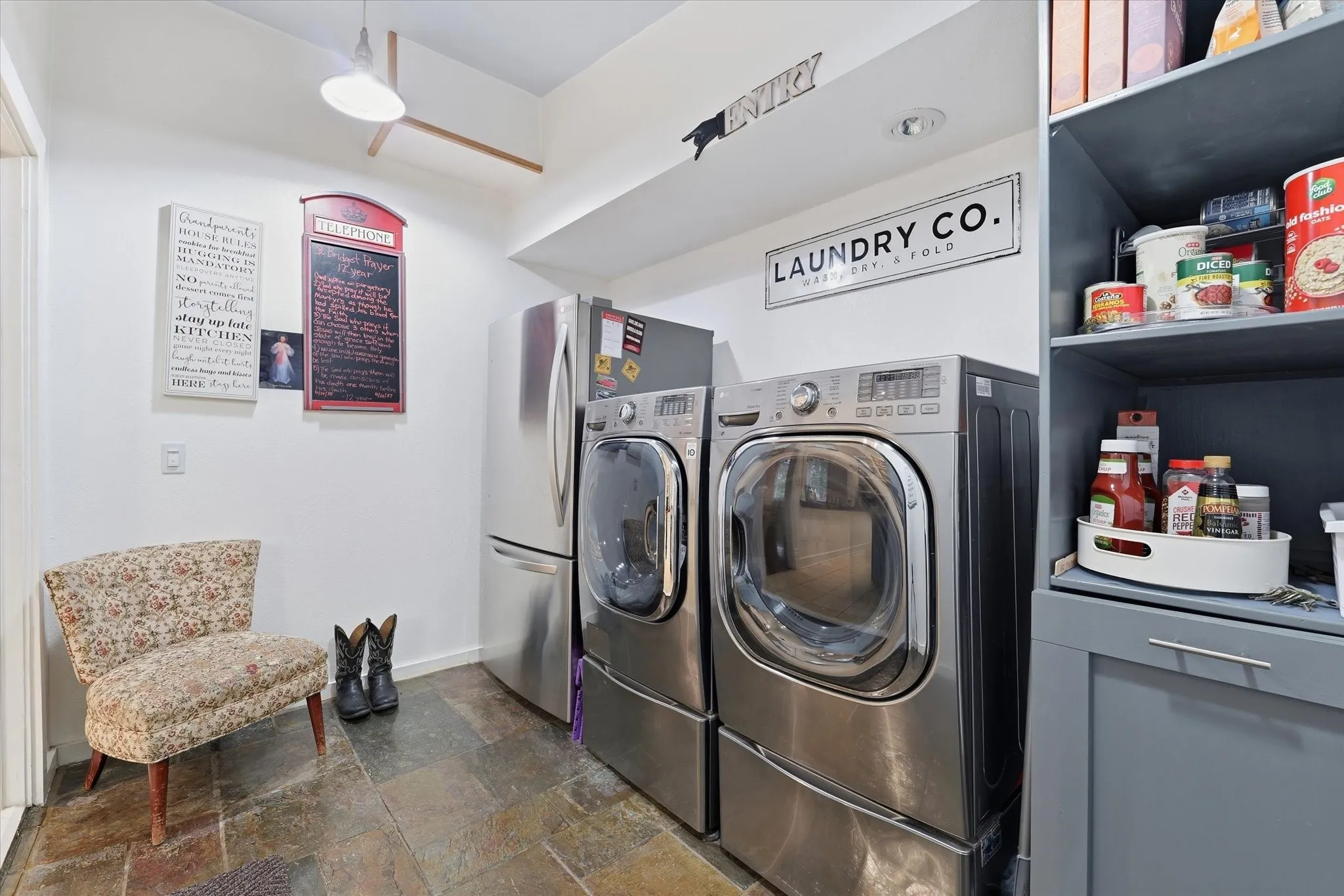 Dedicated laundry area featuring a full-size front-loading washer and dryer, adjacent refrigeration, slate flooring, and built-in shelving with cabinetry as pantry