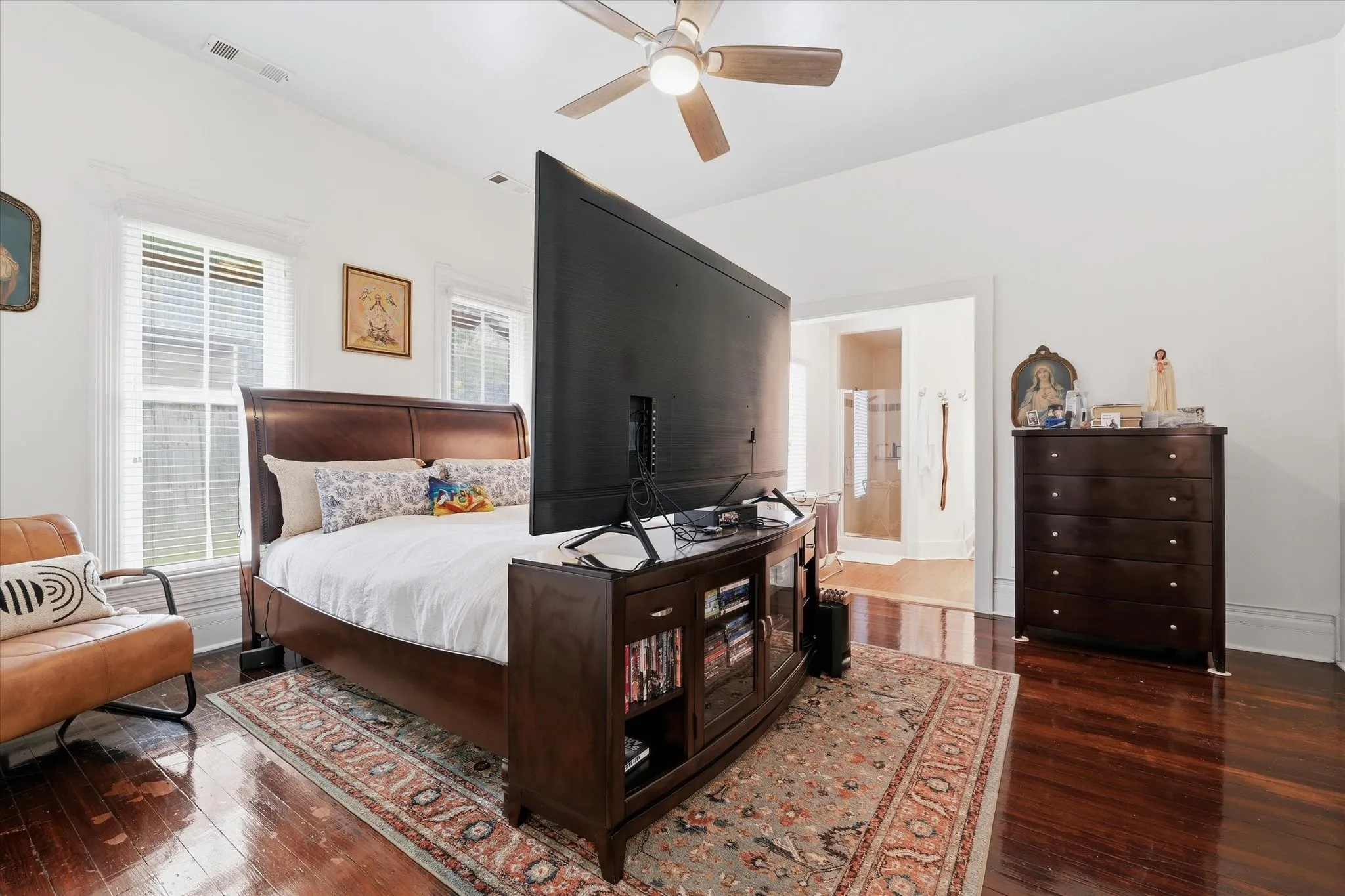 Spacious bedroom featuring rich wood-finish flooring, a ceiling fan, two large windows, and walk-in closet