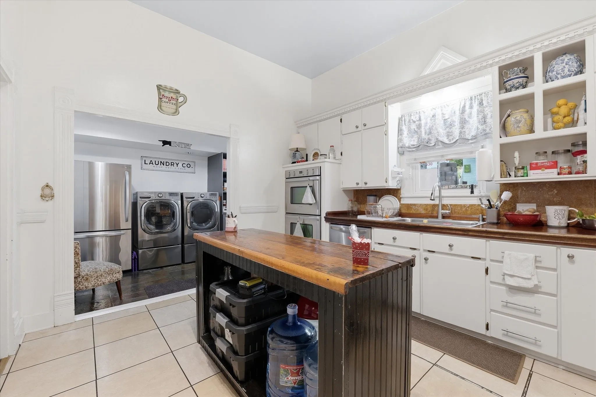 Kitchen featuring white cabinetry, a built-in double oven, open shelving, and a central island with a wood-finish countertop