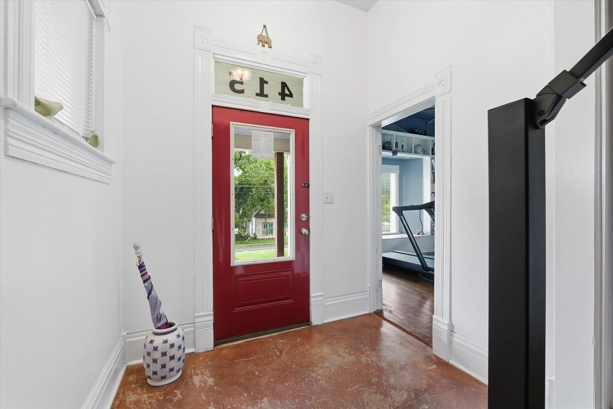 Entryway featuring a red paneled door with glass insert, transom window, and a brown-toned concrete floor