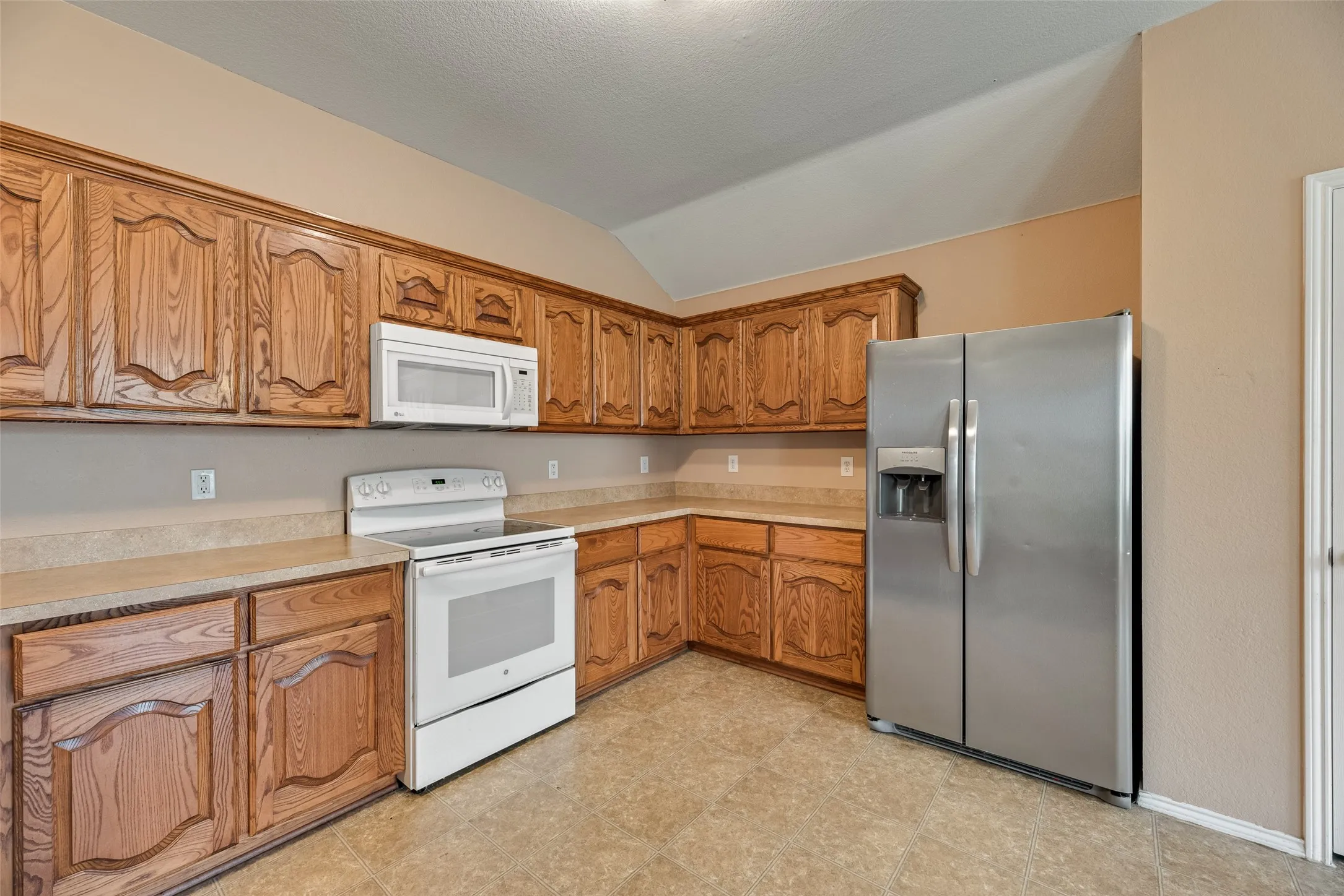 Kitchen featuring extensive wood cabinetry, beige countertops, white electric range with overhead microwave, and a stainless steel side-by-side refrigerator