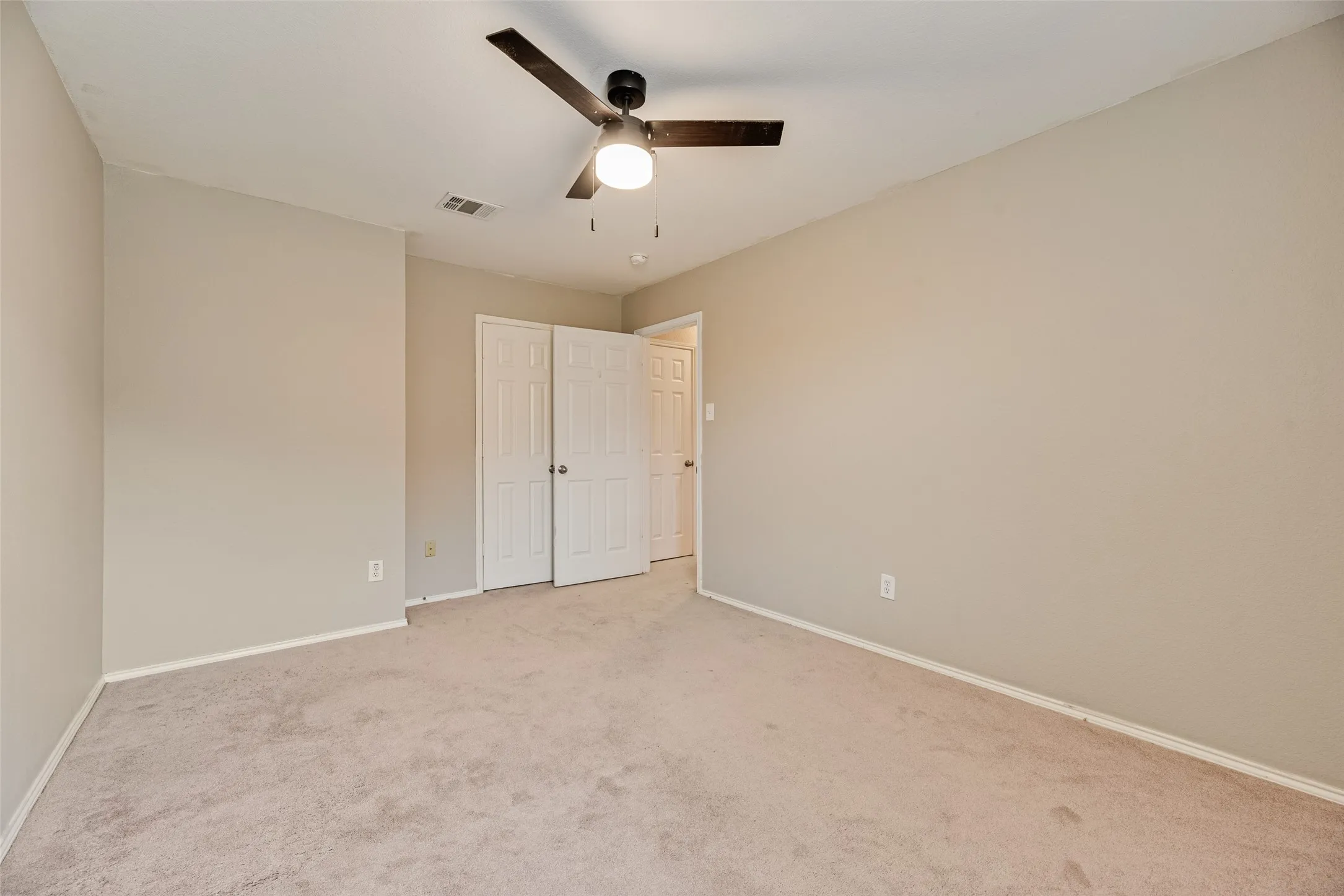 Neutral-toned bedroom featuring wall-to-wall carpeting, a ceiling fan with integrated lighting, and multiple closet doors