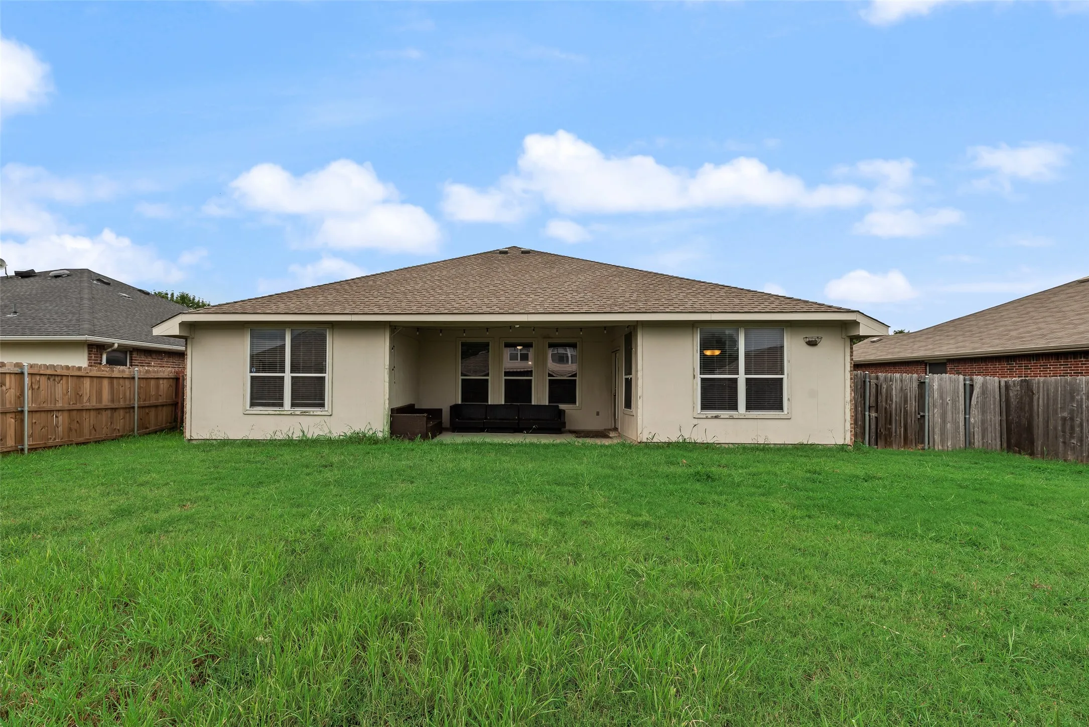 Spacious backyard with a covered patio, tan exterior siding, a shingle roof, and multiple windows