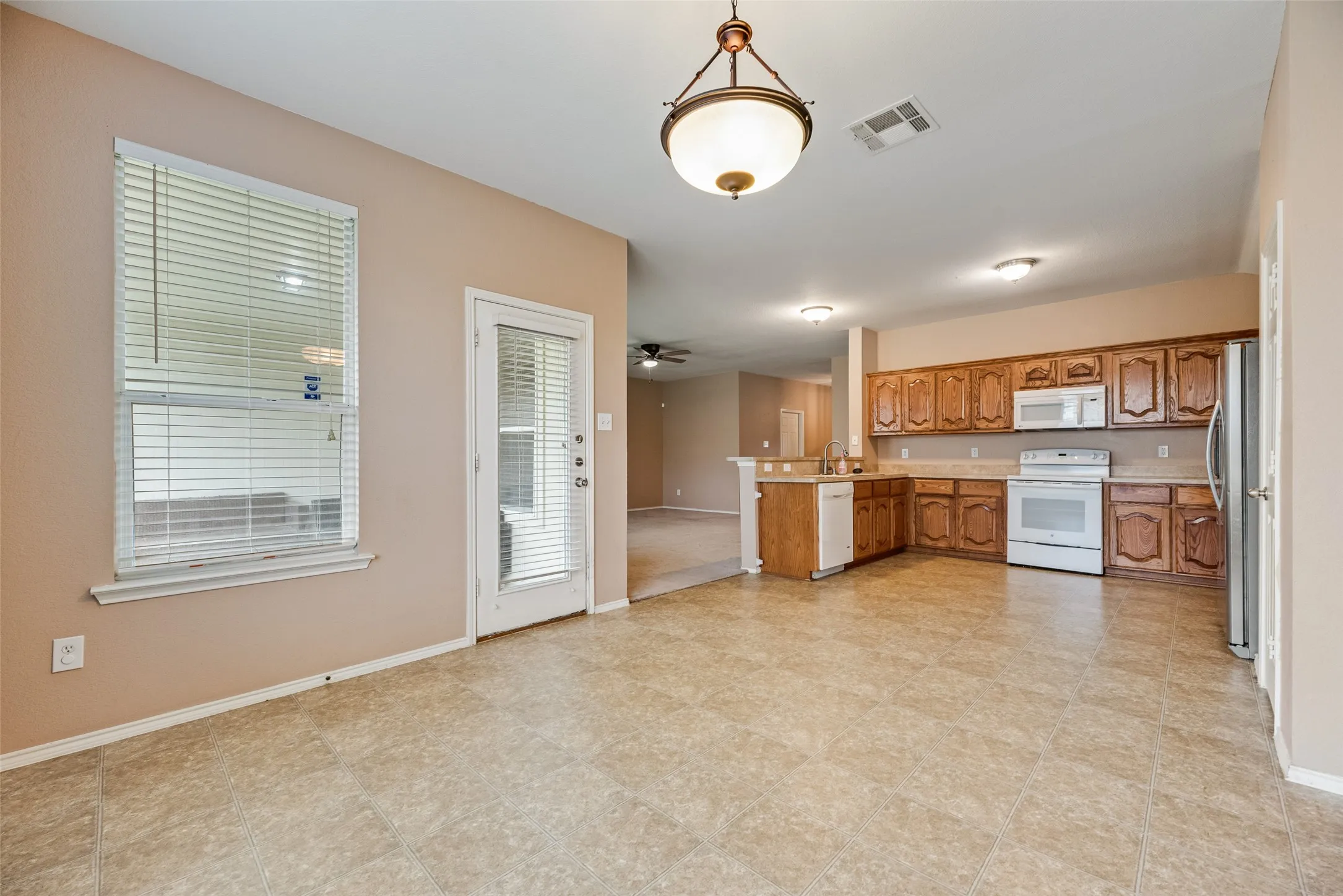 Eat-in kitchen featuring tile flooring, wood cabinetry, white appliances, and a window with blinds