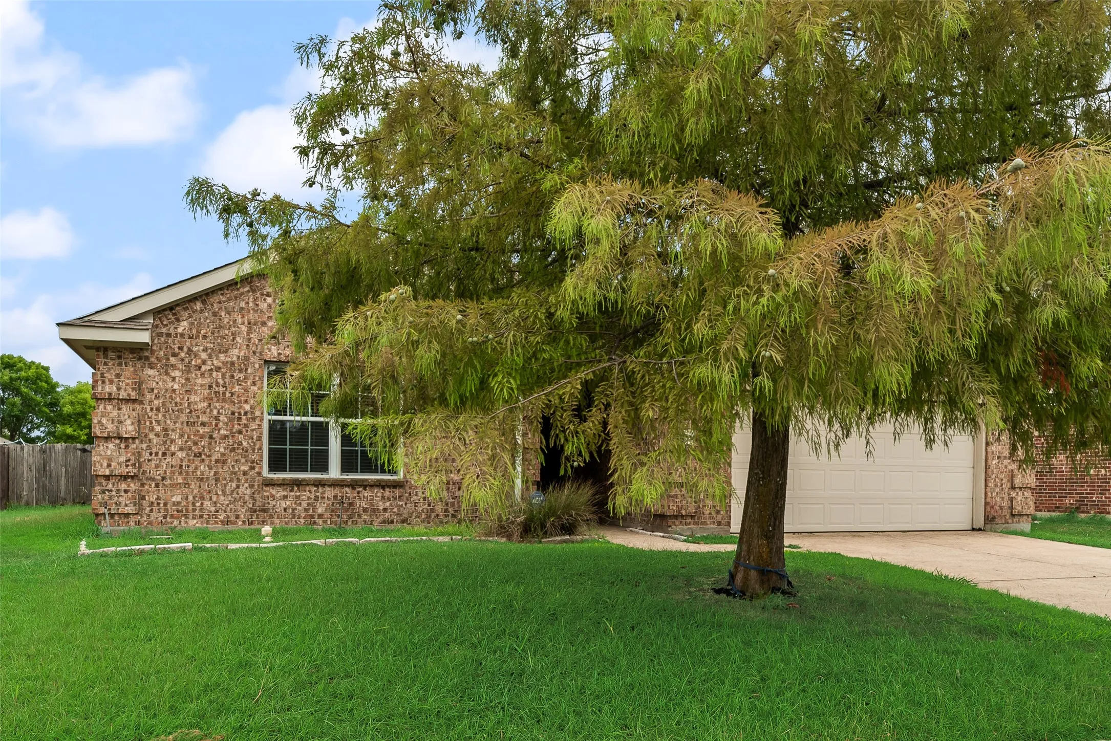Brick exterior residence featuring a front lawn, attached garage, and mature tree
