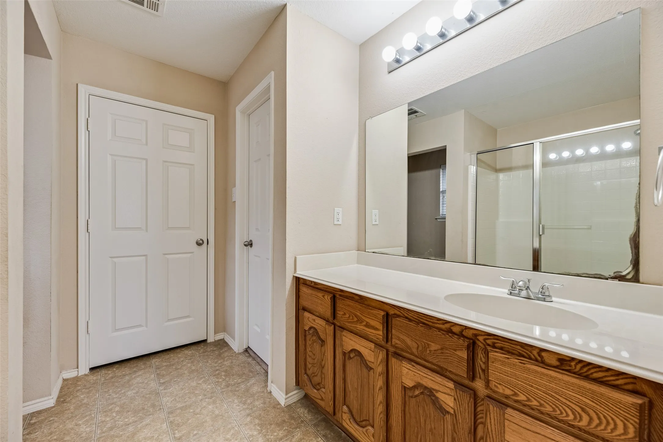 Bathroom vanity featuring a wood-finish cabinet, white countertop with integrated sink, and chrome faucet