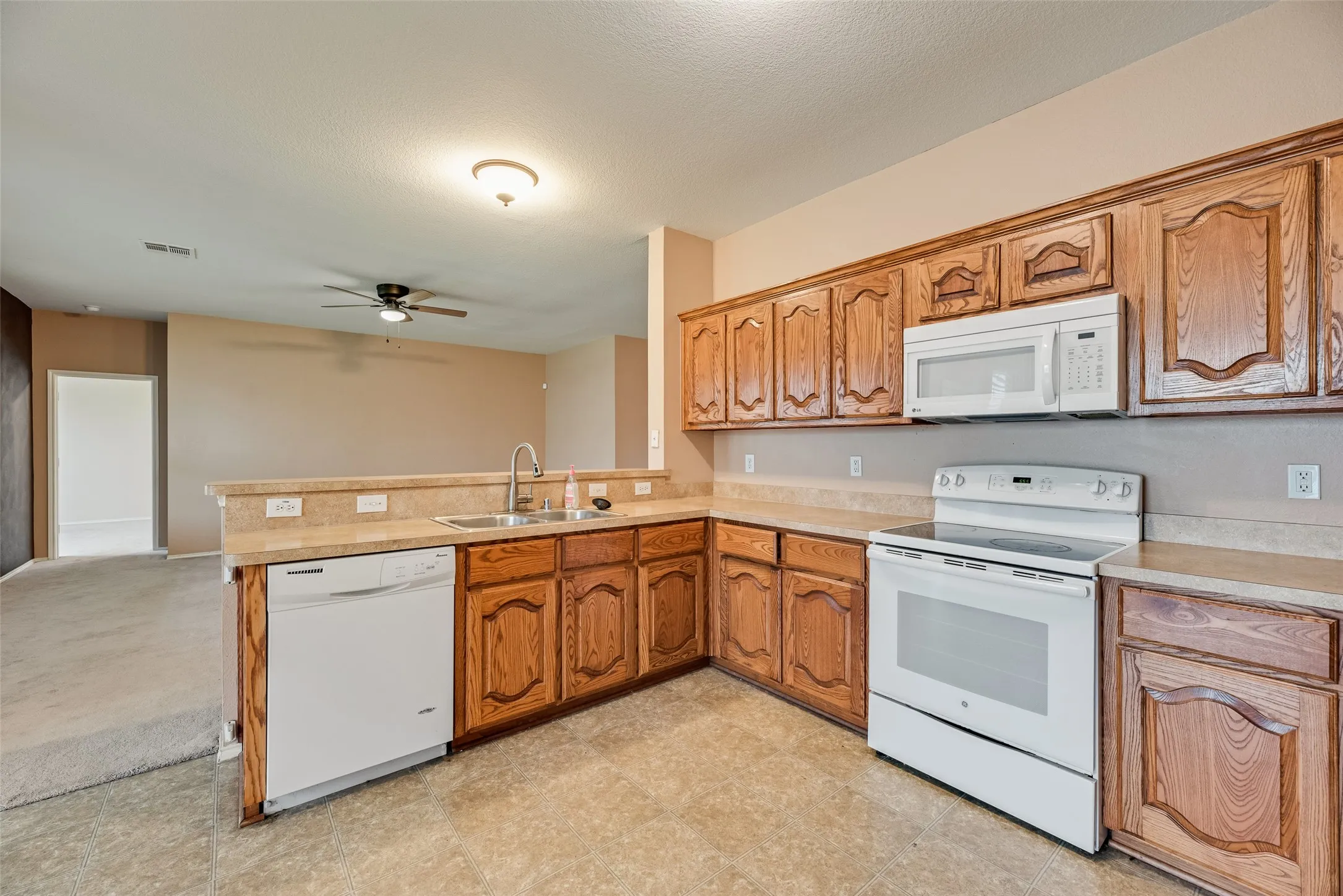 Kitchen featuring wood cabinetry, laminate countertops, a stainless steel sink, a white dishwasher, and a white electric range with an overhead microwave