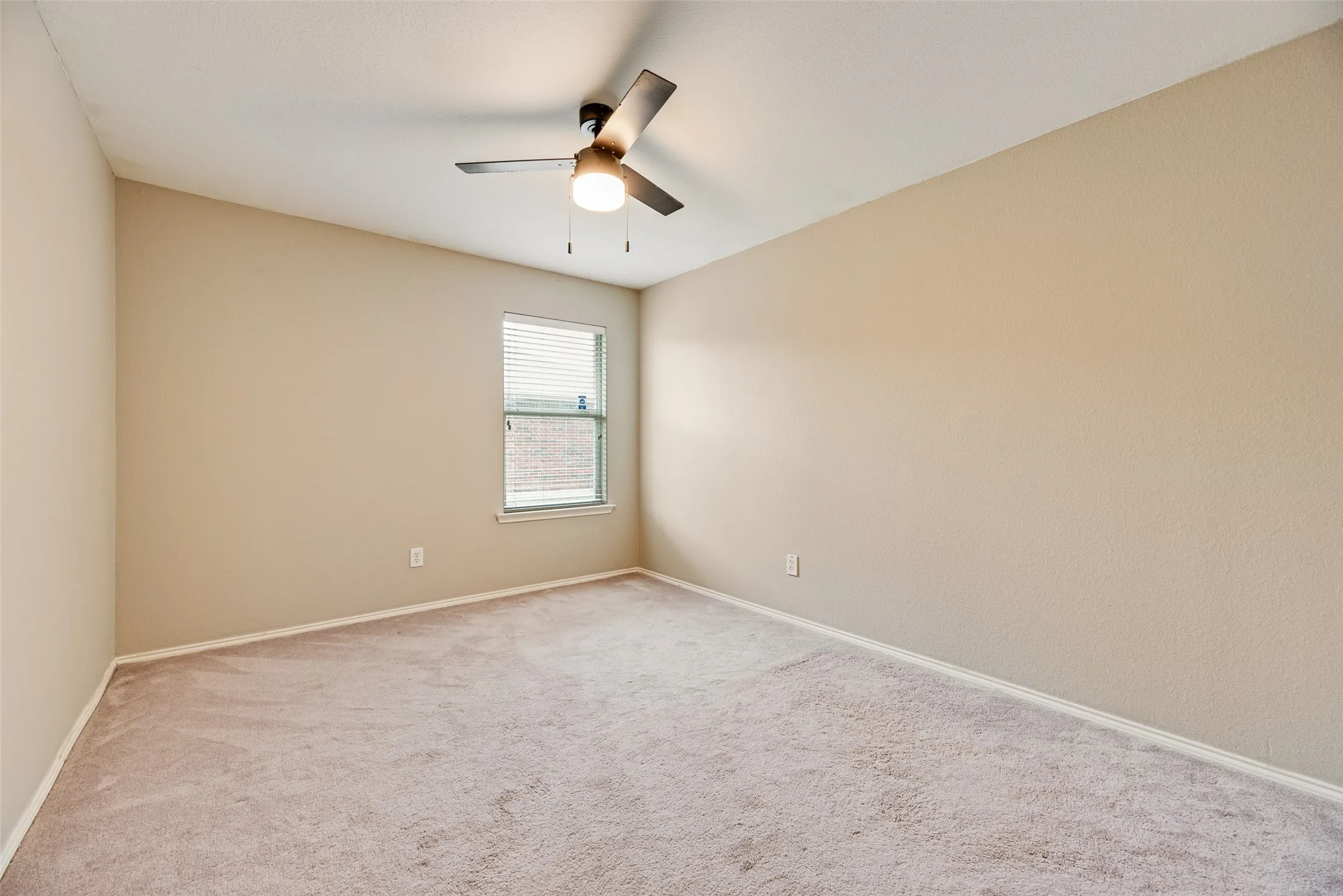 Carpeted room featuring a single window with blinds, a ceiling fan with integrated lighting, textured walls, and white baseboards