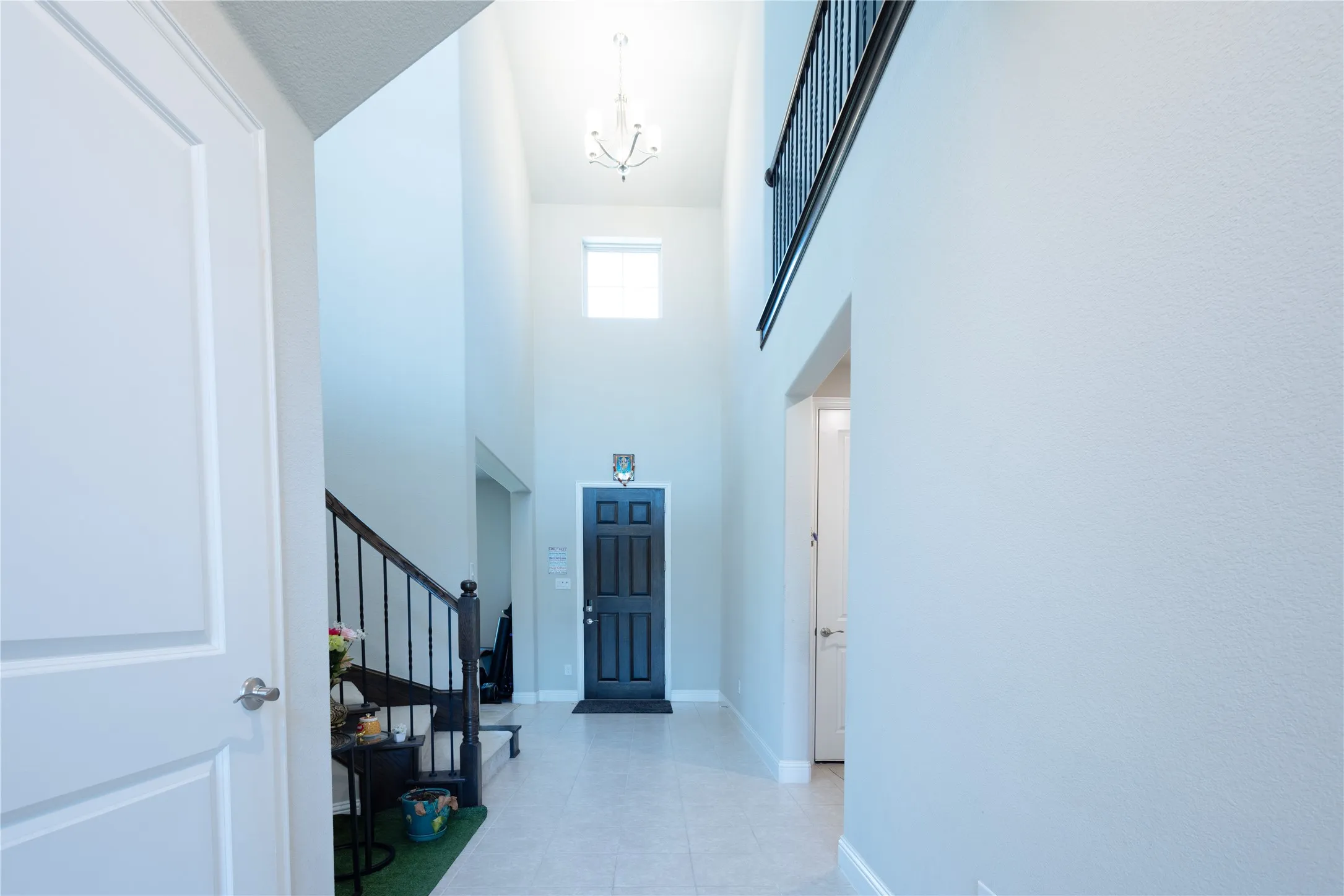 Two-story foyer featuring a dark paneled entry door, light tile flooring, and a stairway with dark wood-finish newel posts and black metal balusters