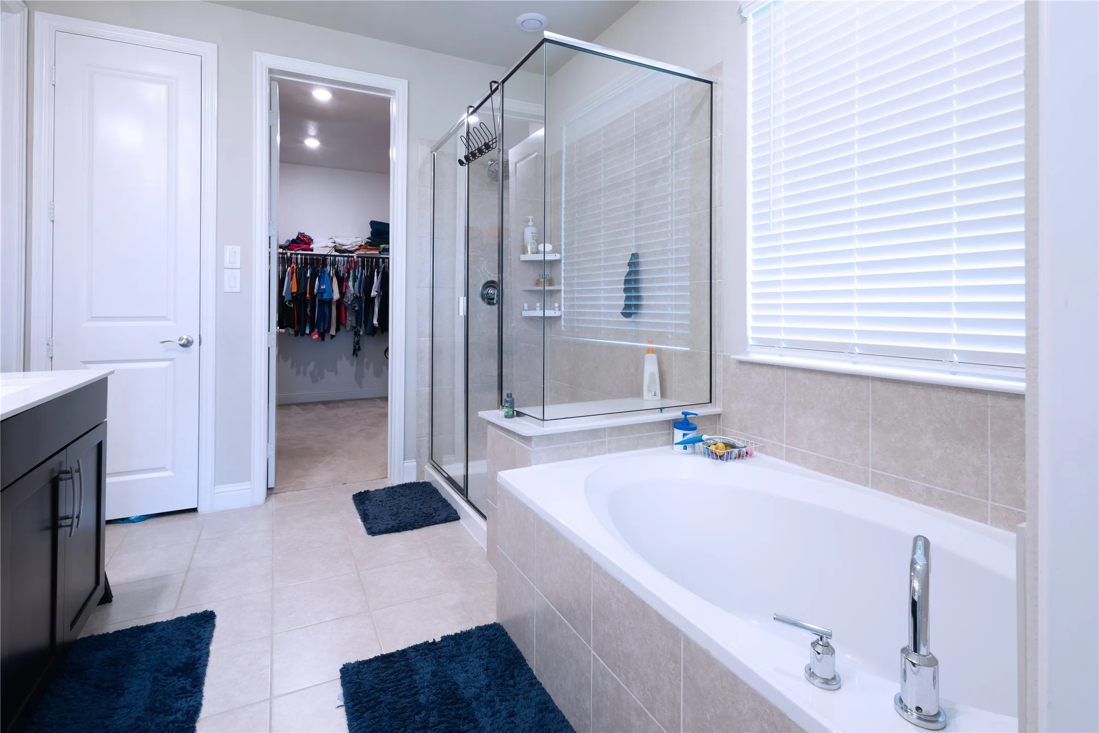 Bathroom featuring a built-in soaking tub, glass-enclosed shower, dark wood-finish vanity with white countertop, and tiled flooring