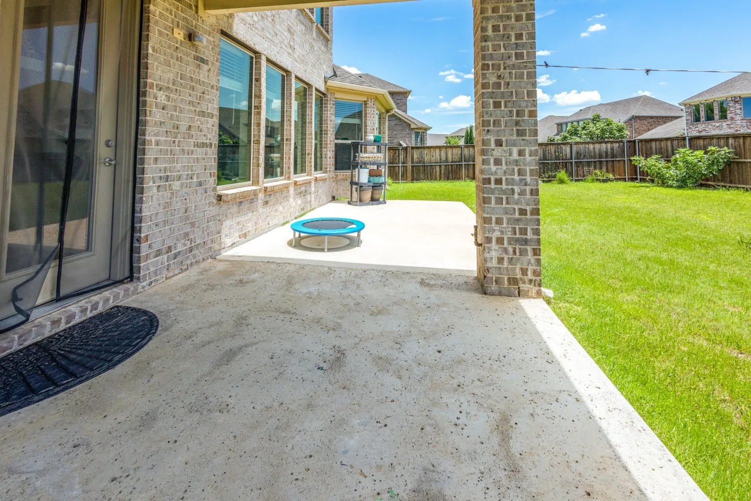 Covered patio with a concrete slab, brick support columns, and an exterior door providing access to the interior