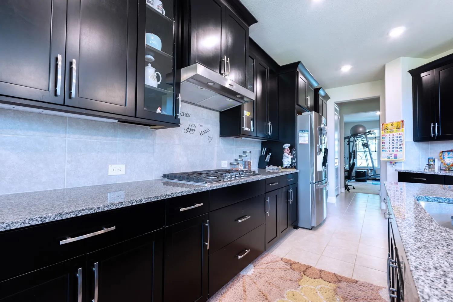 Kitchen featuring dark cabinetry with brushed nickel hardware, granite countertops, tile flooring, and a stainless steel range hood