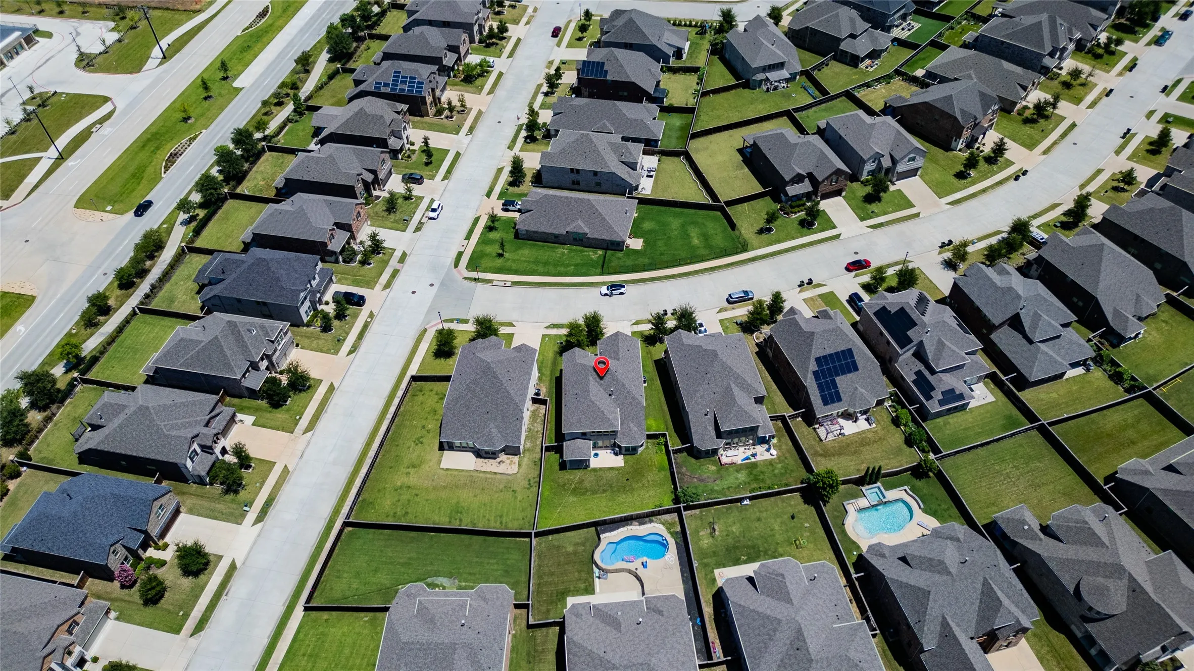 Modern residential neighborhood featuring single-family homes with dark roofs, green lawns, and concrete driveways