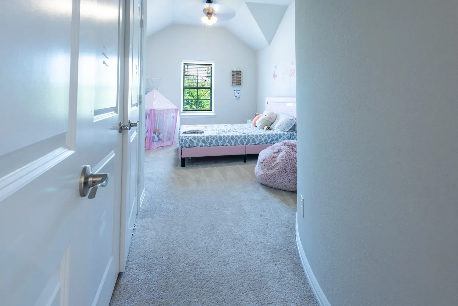 Carpeted bedroom featuring a vaulted ceiling with a ceiling fan, a window, and a white interior door