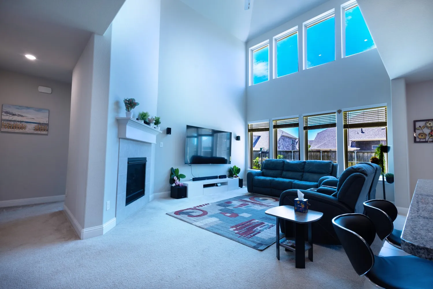 Two-story living area featuring a fireplace with a white mantel, a wall of upper transom windows, and lower-level windows with blinds