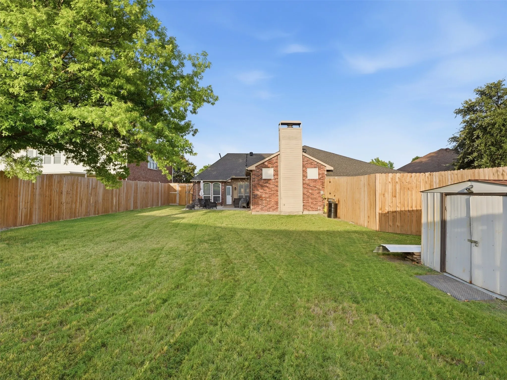 Expansive backyard featuring a large green lawn, full wood privacy fencing, and a brick exterior home with a back patio