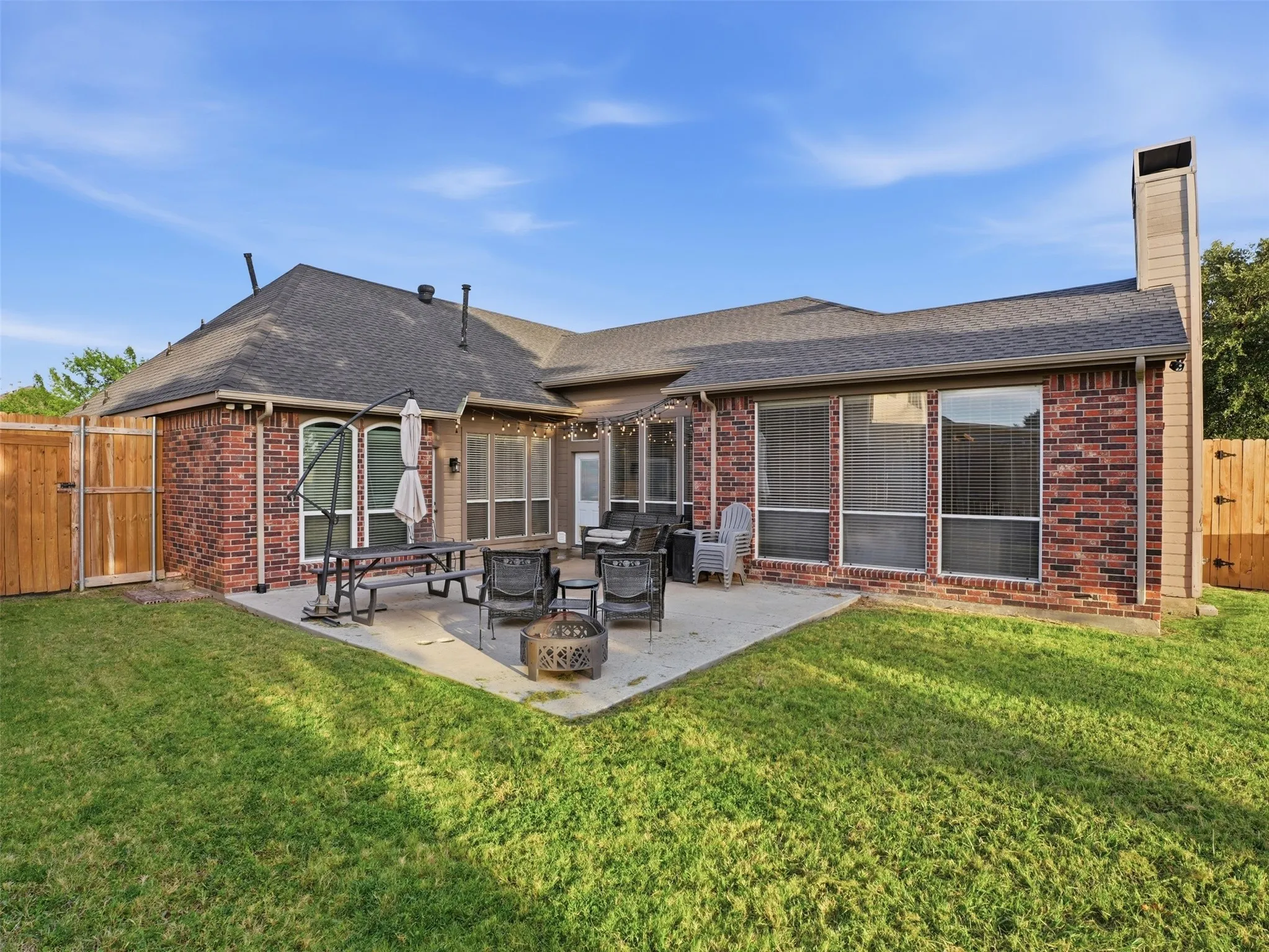 Expansive backyard featuring a concrete patio, a full brick exterior, a tall exterior chimney, and a wooden privacy fence