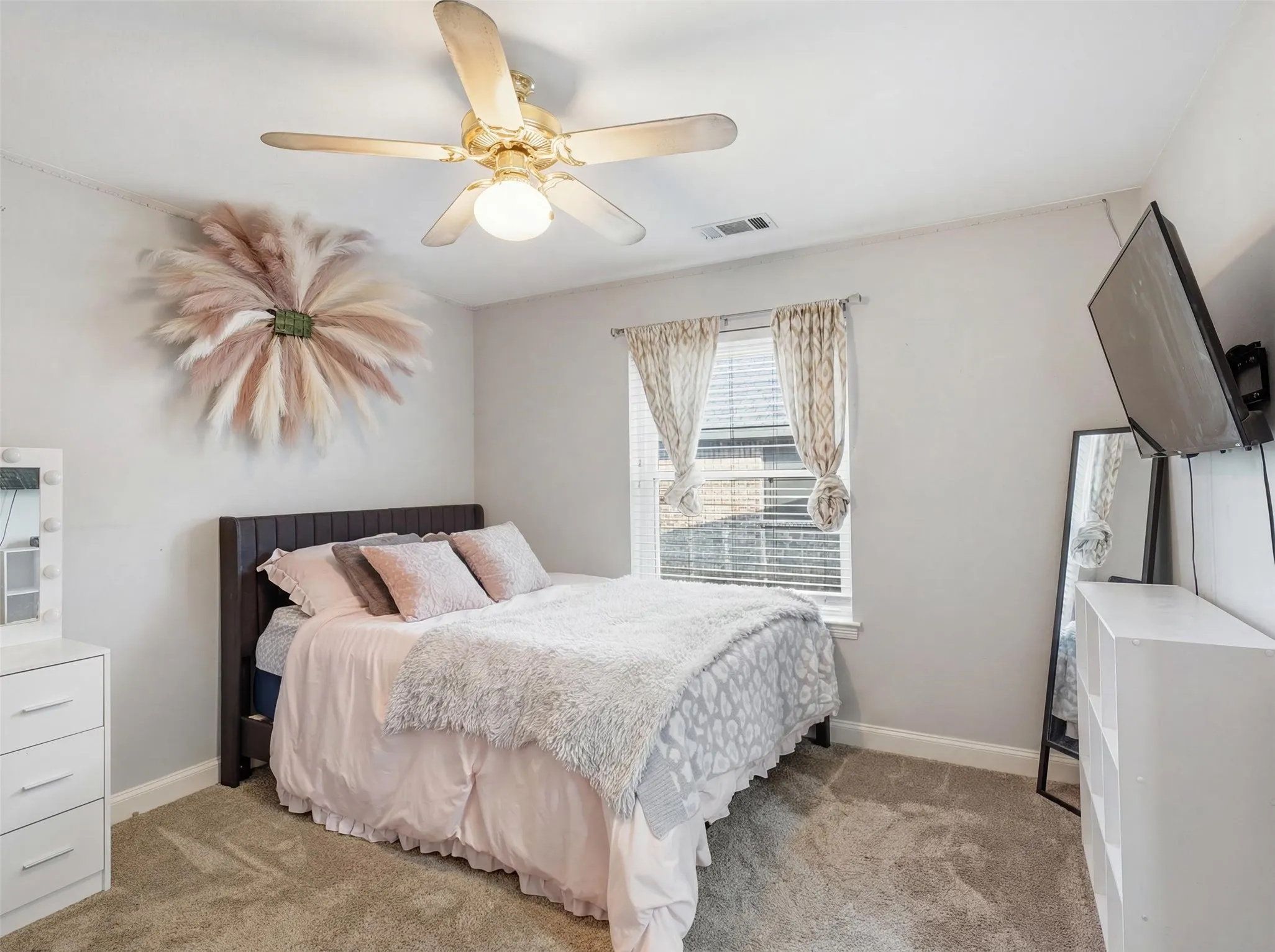 Carpeted room featuring a ceiling fan with integrated lighting, a window with blinds and drapes, and a dark wood-finish headboard