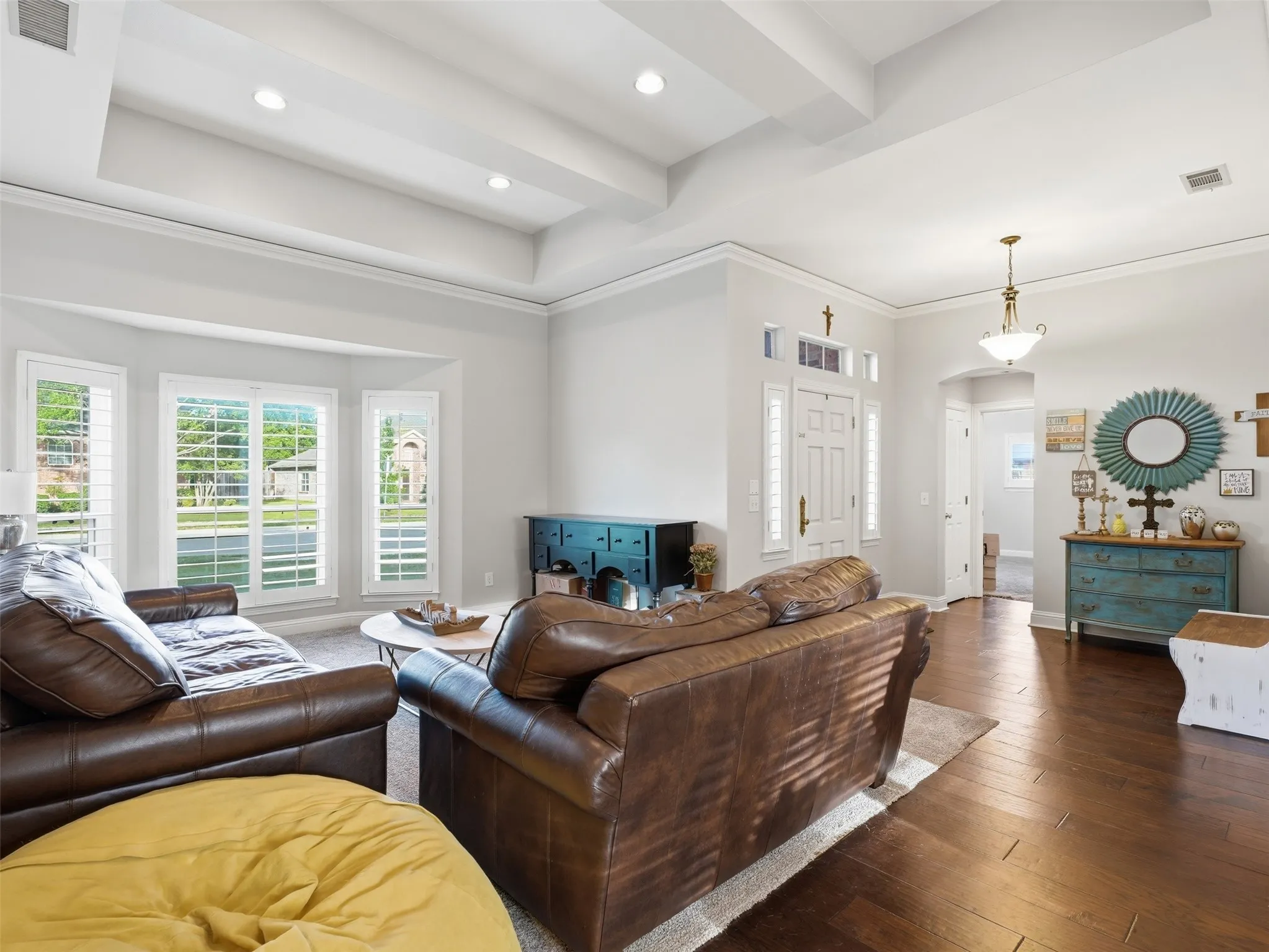 Spacious formal living area featuring a tray ceiling with recessed lighting, wood-finish flooring, and a bay window with plantation shutters