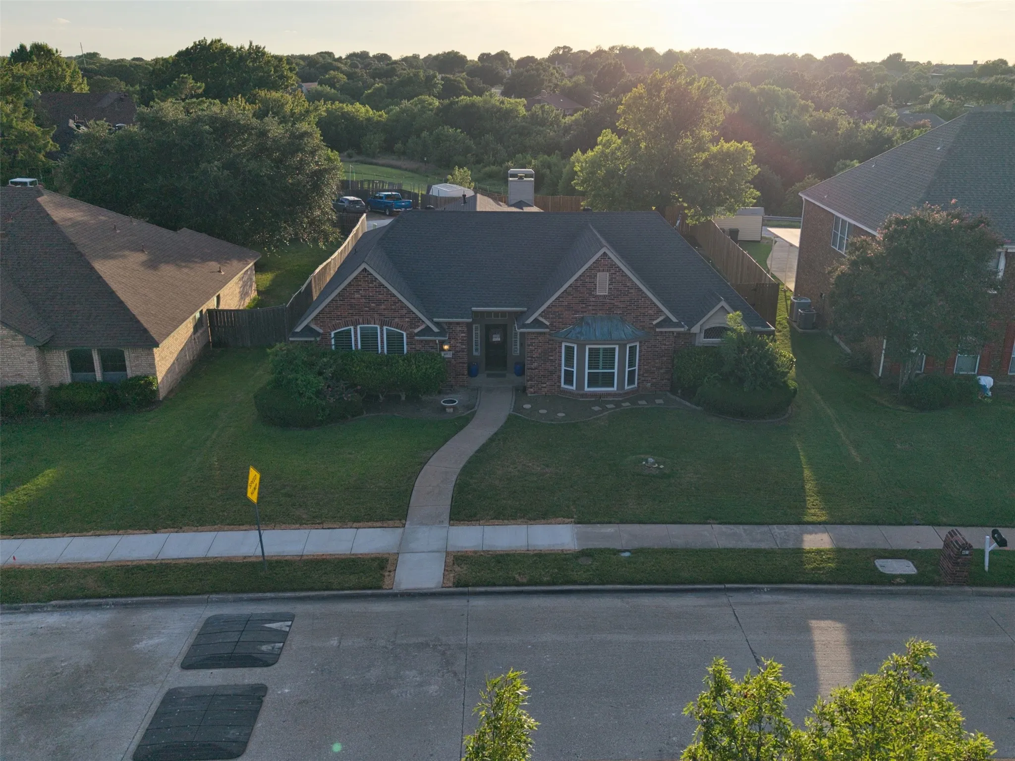 Brick and stone exterior featuring a bay window, a concrete walkway, mature landscaping, and a dark shingle roof