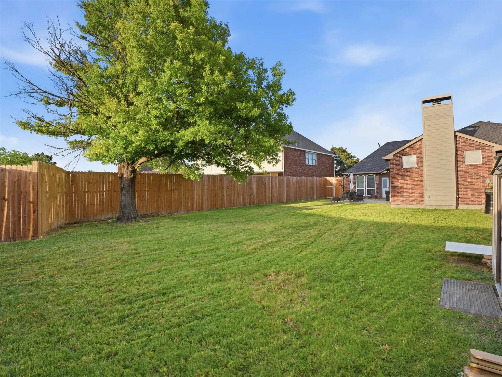Expansive backyard featuring a manicured lawn, established tree, wood privacy fencing, and a brick exterior with a chimney