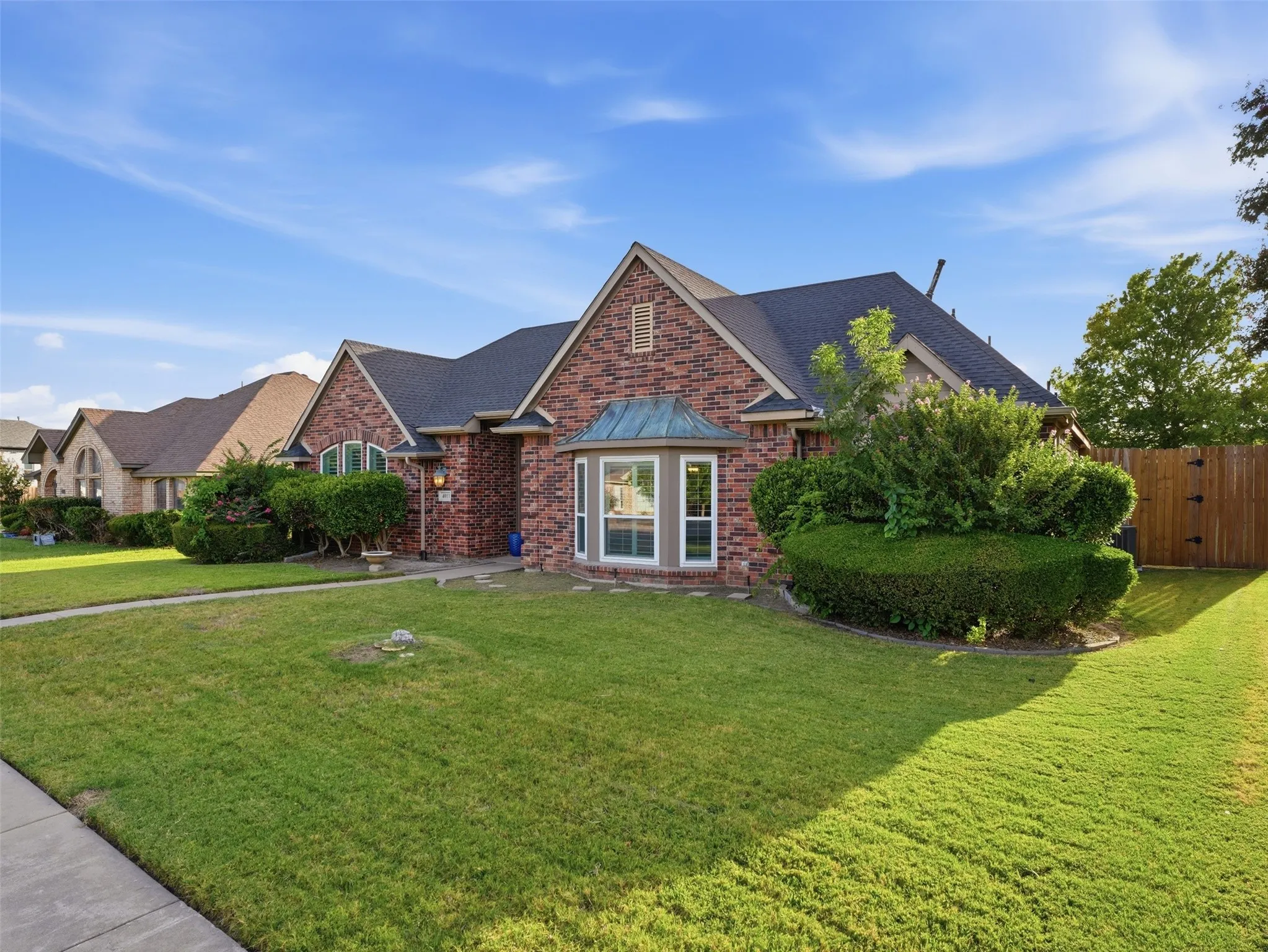 Brick facade residence featuring a prominent bay window with a copper-toned awning, arched entry window, dark shingle roofing, and a privacy fence