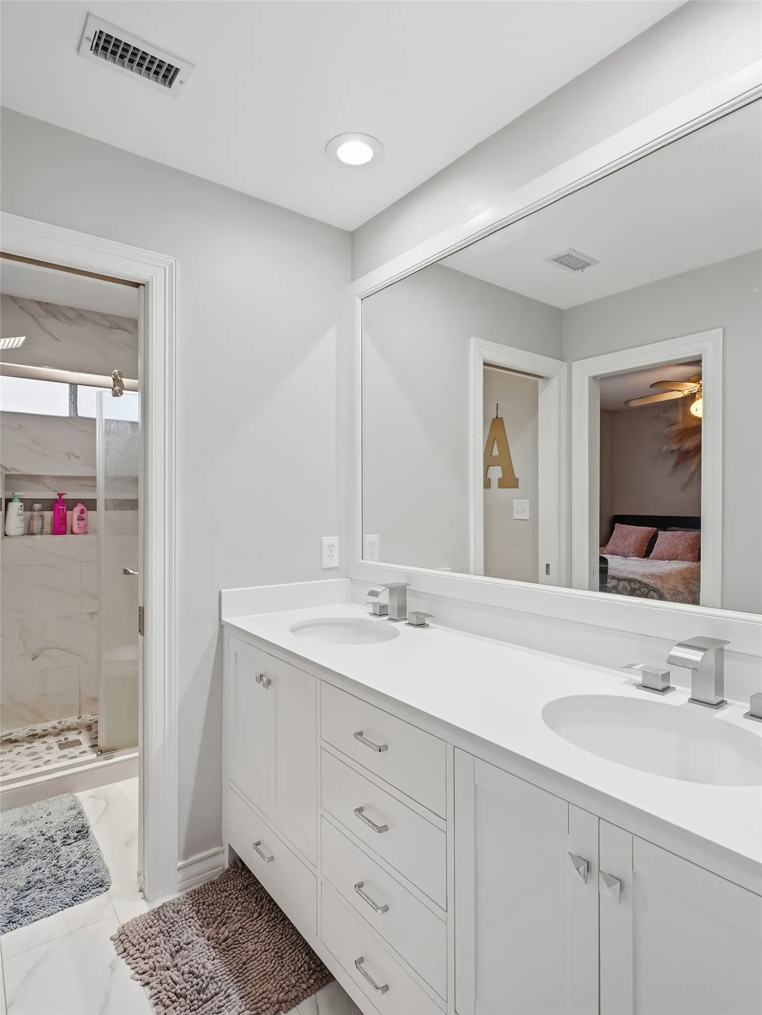 Bathroom vanity in guest bathroom featuring dual under-mount sinks, white cabinetry with chrome hardware, and a framed mirror