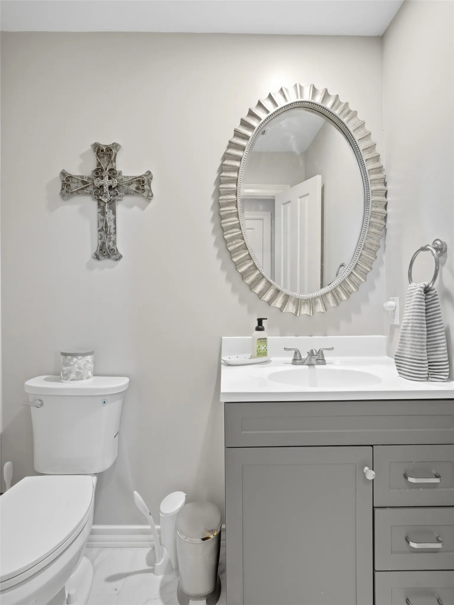 Powder room or guest half bath featuring a gray vanity with a white countertop and integrated sink, a fluted oval mirror, and light gray wall paint