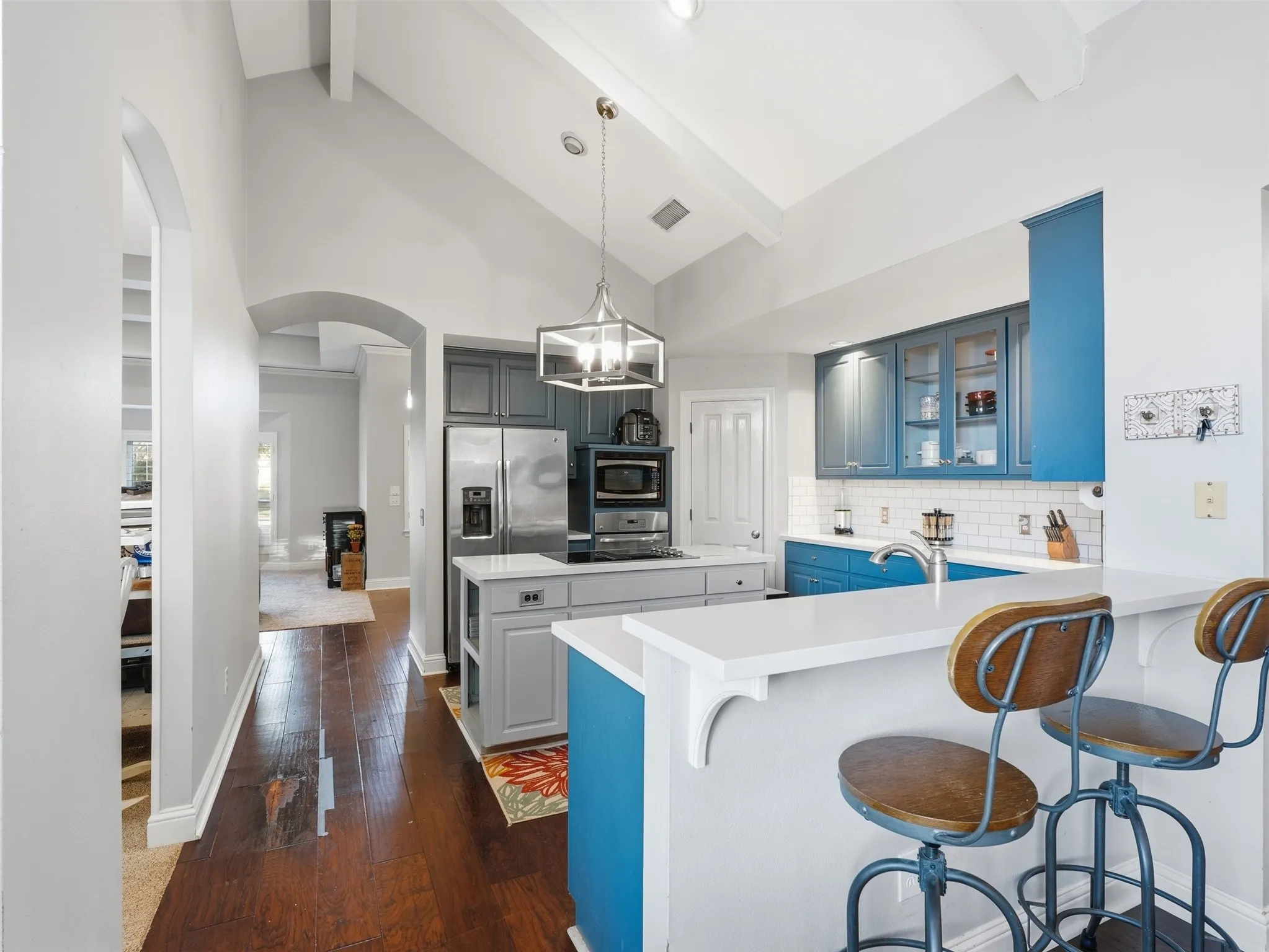 Vaulted ceiling kitchen featuring a central island, stainless steel appliances, vibrant blue and gray cabinetry, and wood-finish flooring