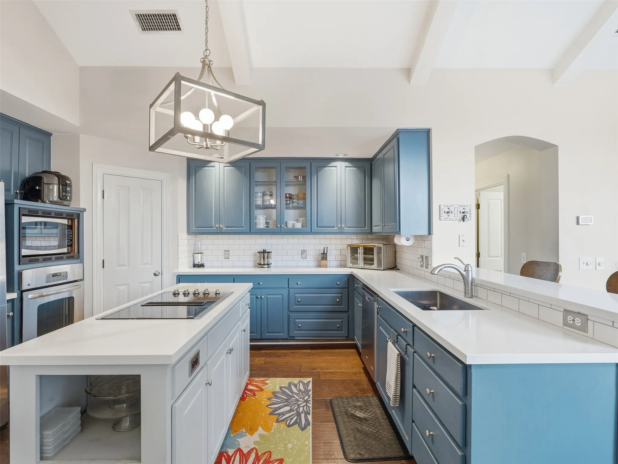 Kitchen featuring a center island with built-in cooktop, blue cabinetry, light countertops, subway tile backsplash, and wood-finish flooring