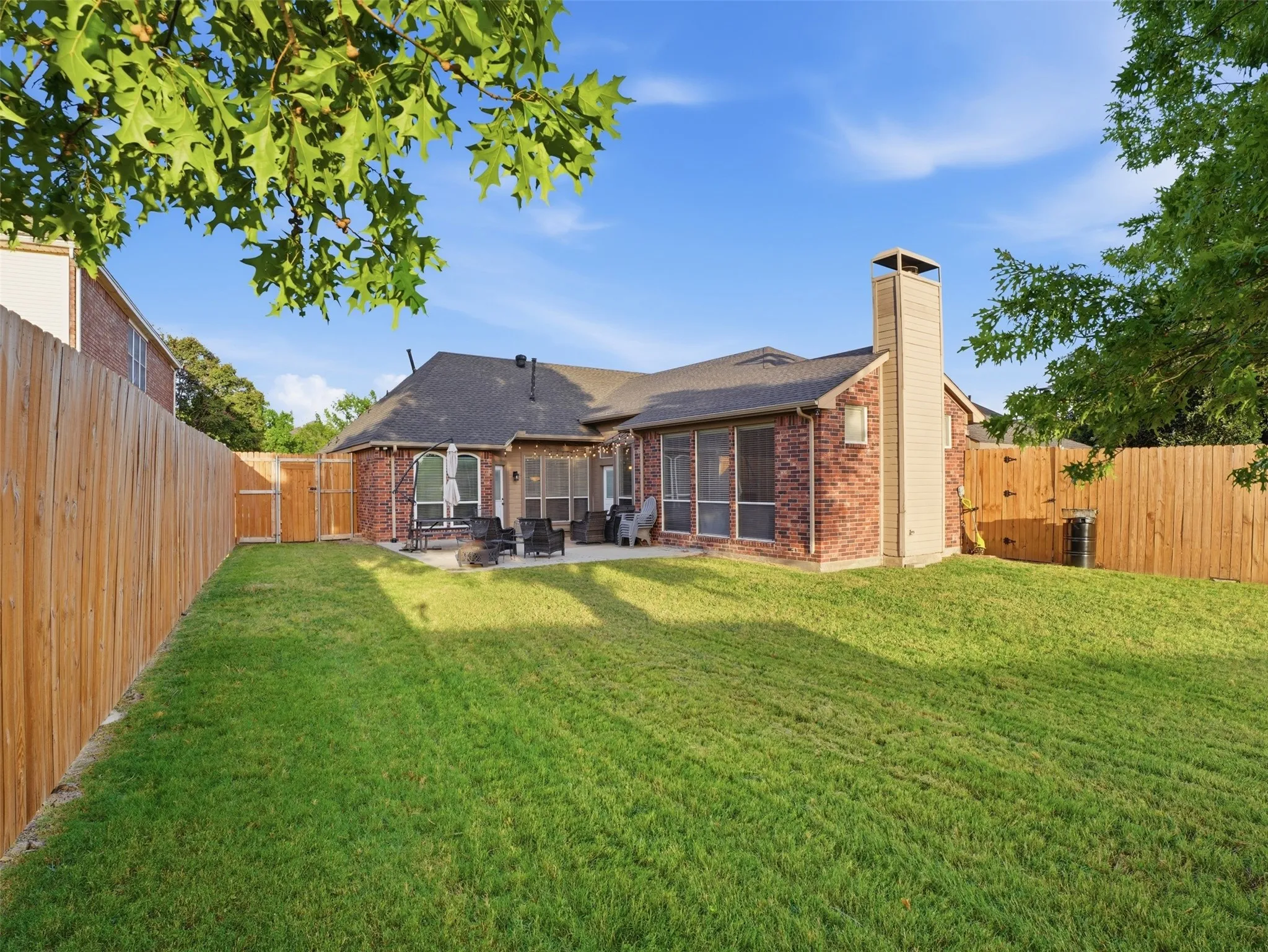 Expansive backyard featuring a manicured lawn, full privacy fencing, and a brick-and-siding exterior