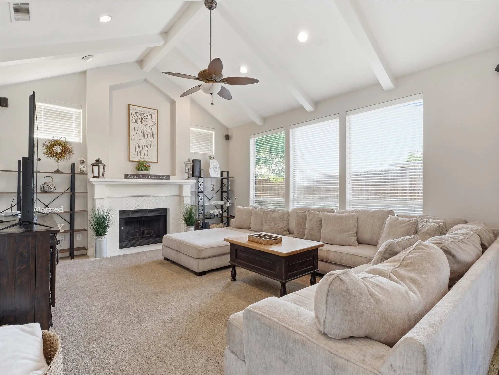 Living room featuring a vaulted ceiling with exposed beams, ceiling fan, recessed lighting, and a fireplace with a white mantel and tile surround