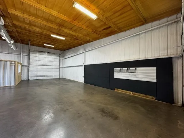 Spacious commercial interior featuring a high wood-paneled ceiling with fluorescent lighting, polished concrete flooring, and metal panel walls