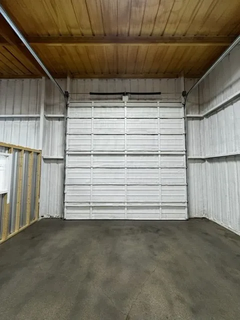Industrial-style interior featuring a white sectional garage door, corrugated metal walls, and a wood-finish ceiling