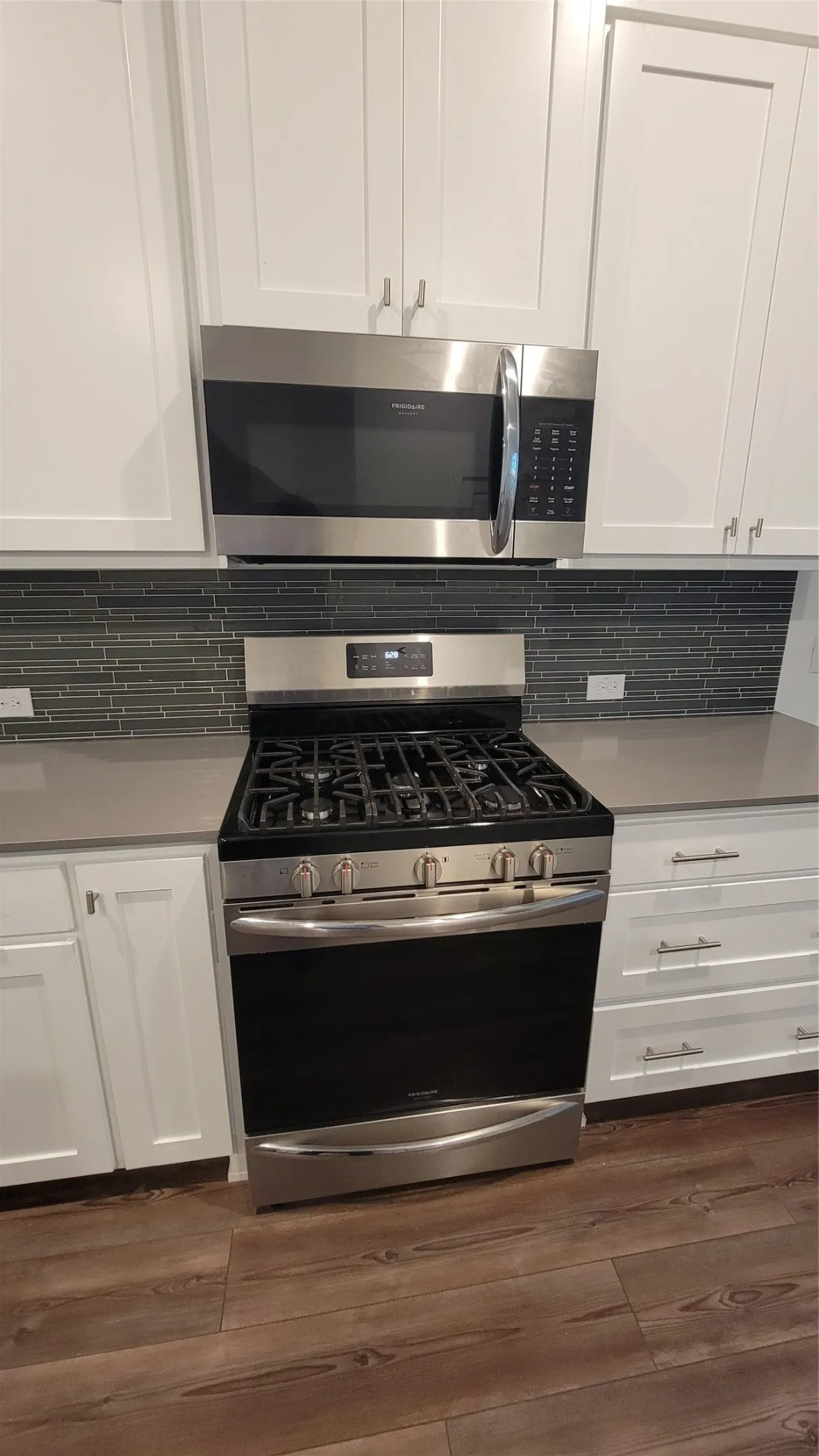 Kitchen featuring dark hardwood / wood-style flooring, white cabinetry, tasteful backsplash, and gas range