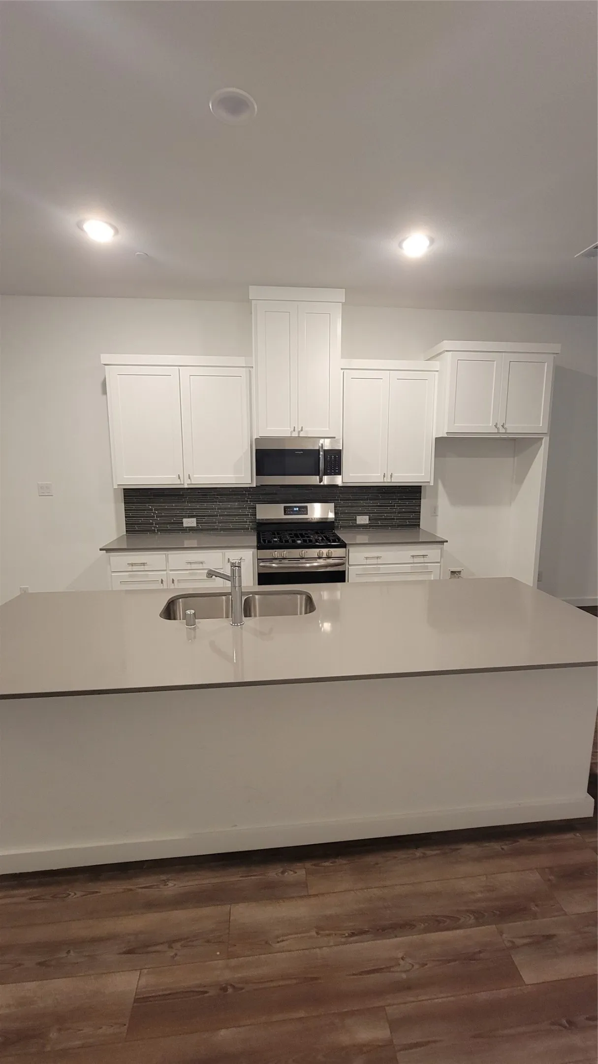 Kitchen featuring an island with sink, dark hardwood / wood-style flooring, stainless steel range with gas stovetop, and white cabinetry