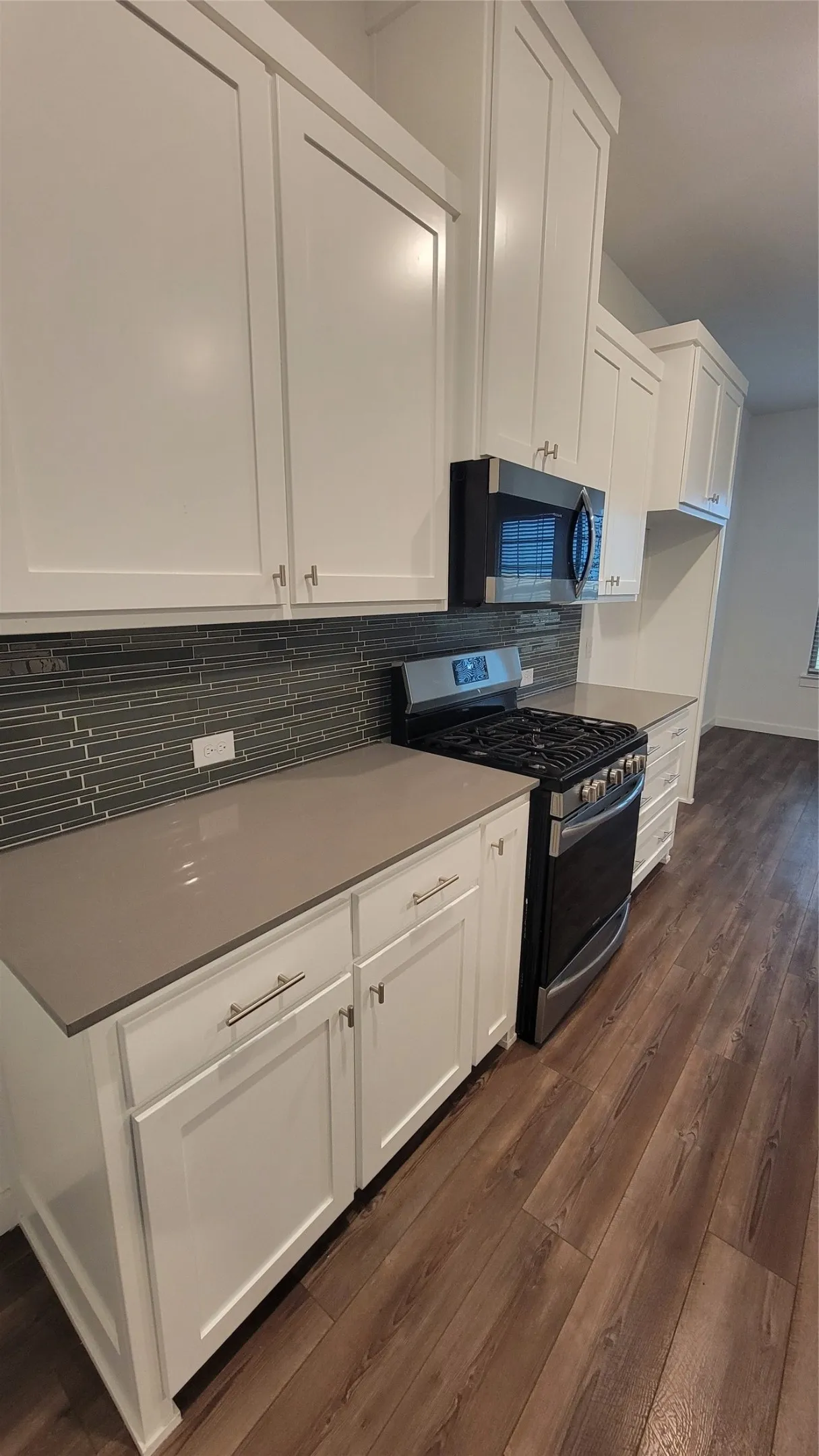 Kitchen with white cabinets, tasteful backsplash, dark hardwood / wood-style floors, and range