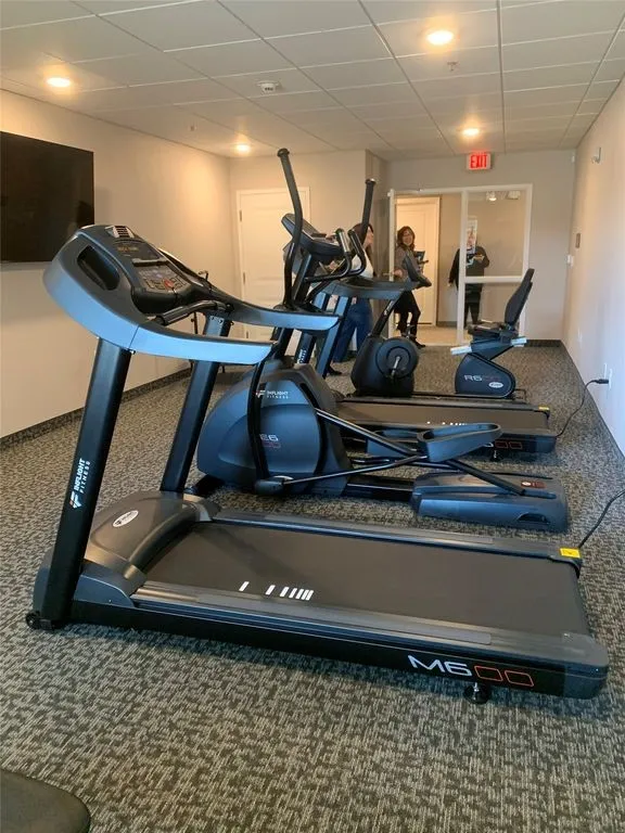 Fitness center featuring multiple exercise machines, recessed lighting, drop ceiling, wall-mounted television, and patterned carpet