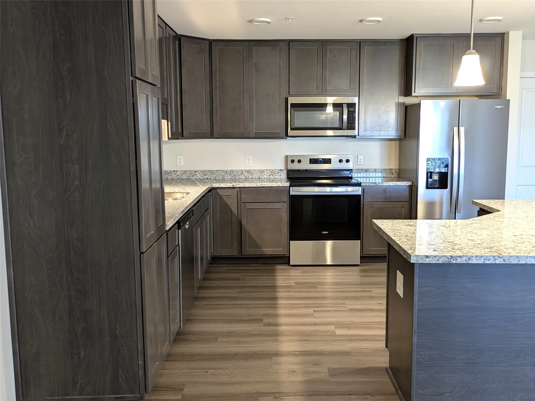 Modern kitchen featuring dark wood-finish cabinetry, light speckled countertops, and stainless steel appliances