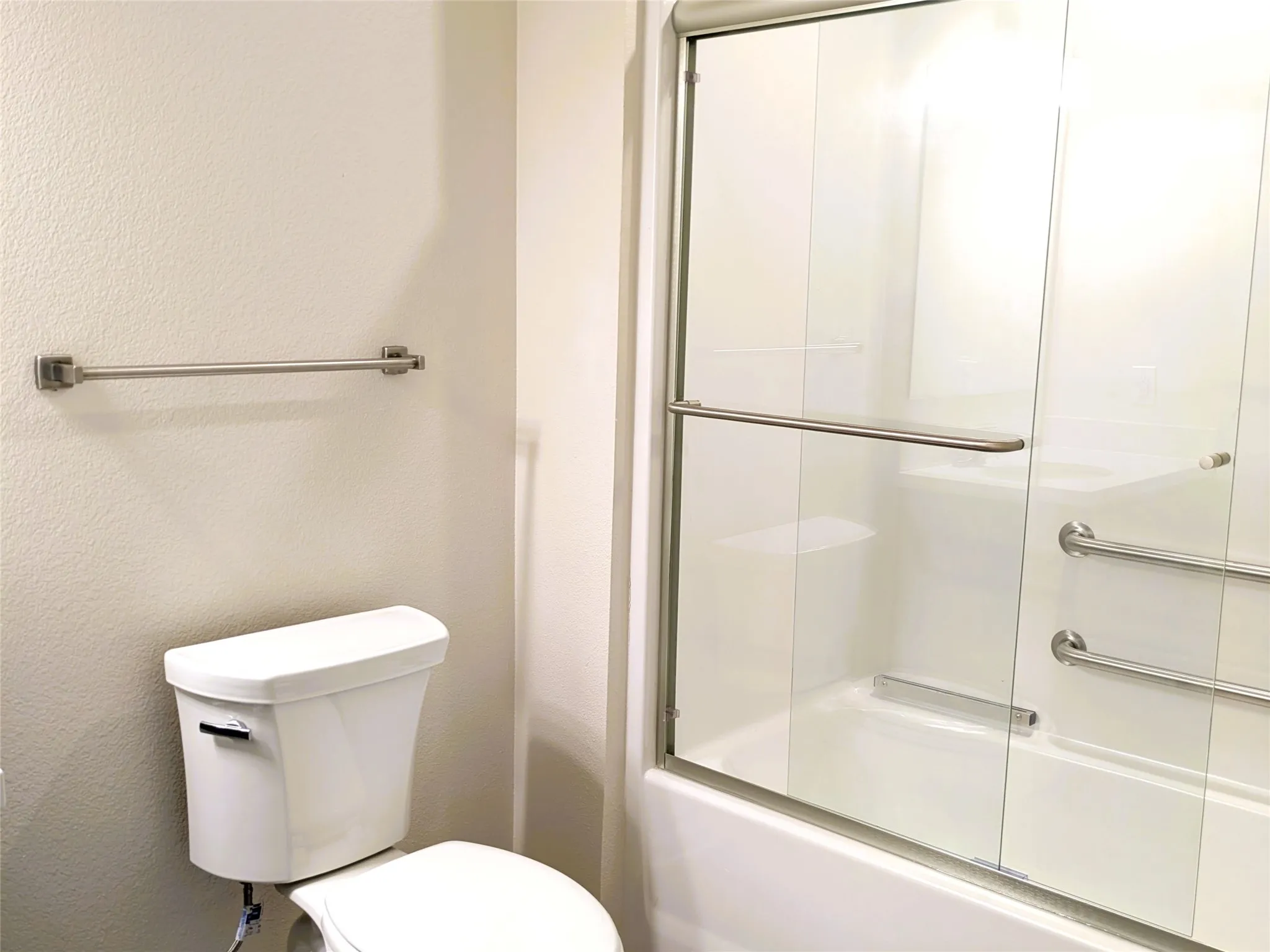Bathroom featuring a white tub with a clear glass enclosure, brushed nickel hardware, and multiple grab bars