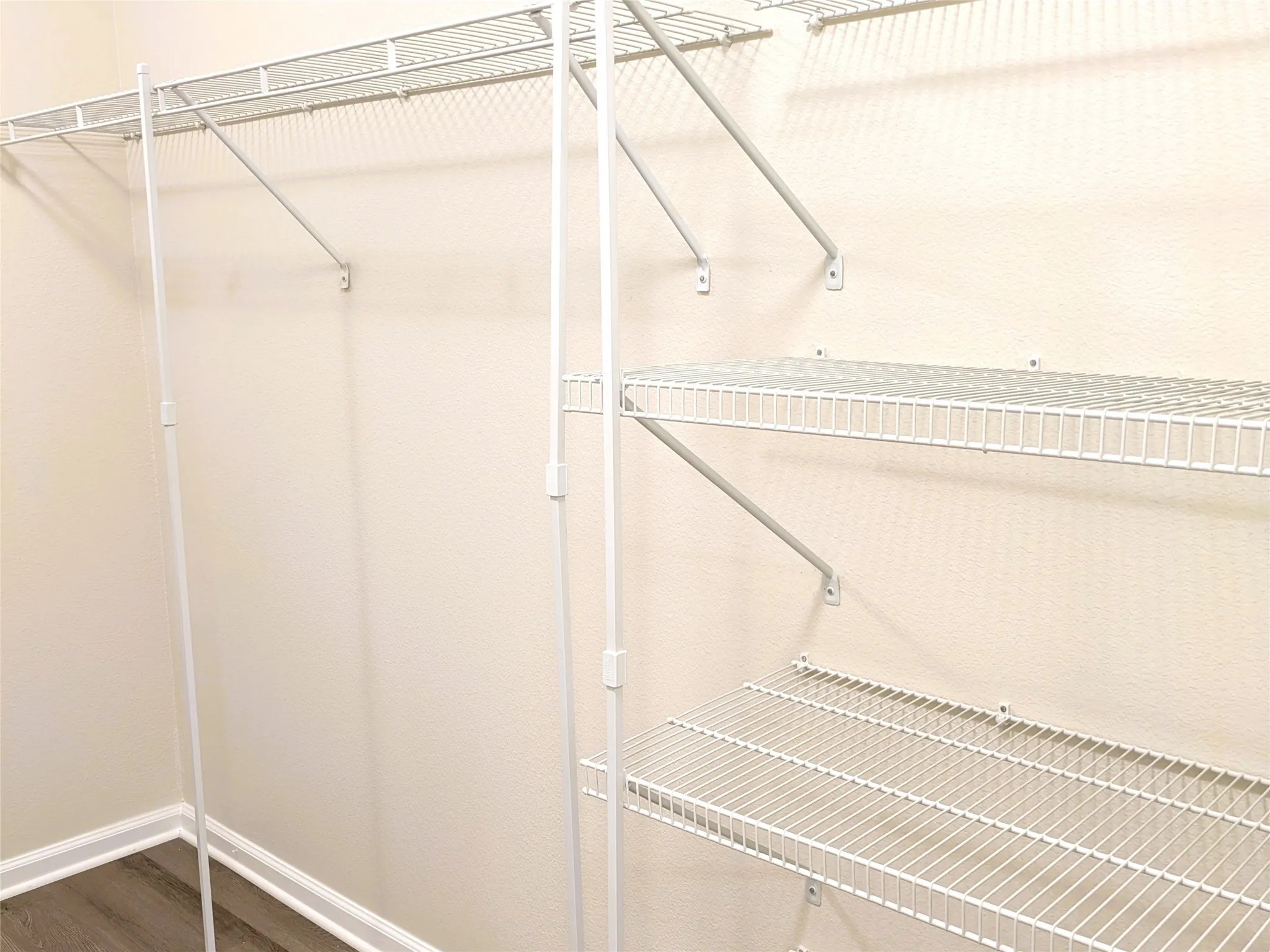 Closet system featuring multiple wire shelves, hanging rods, and wood-finish flooring