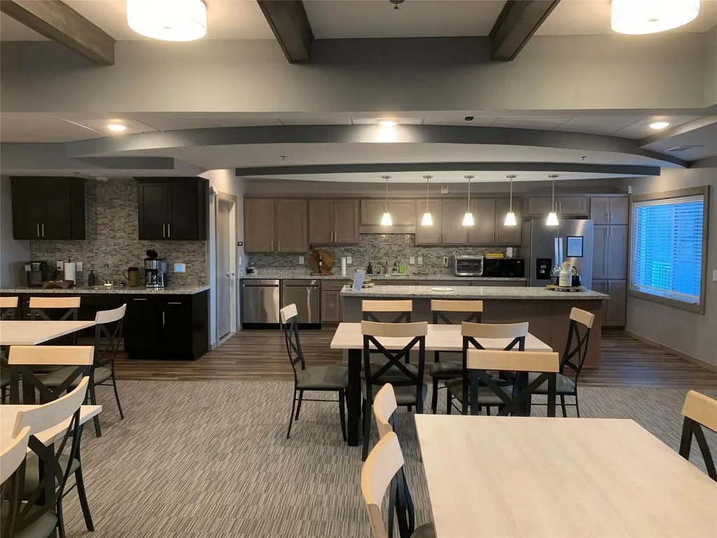 Spacious common area featuring a full kitchen with stainless steel appliances, an island with pendant lighting, wood-finish flooring, and exposed ceiling beams