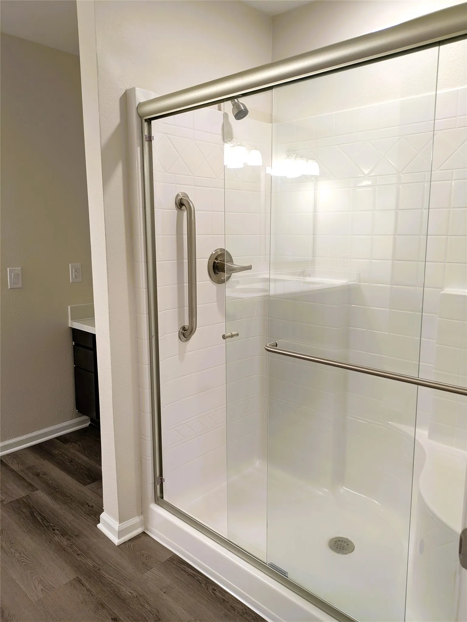 Glass-enclosed shower featuring white subway tile, a brushed nickel showerhead, and a grab bar