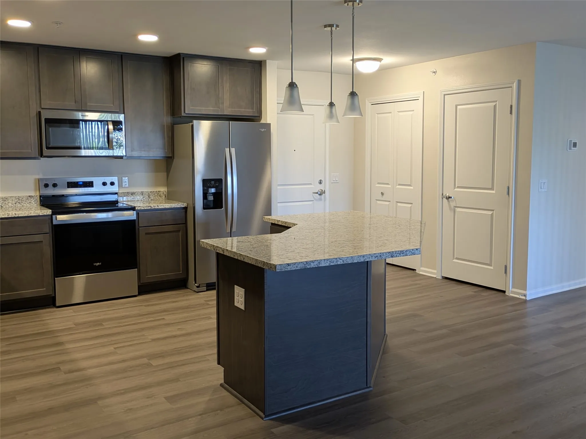 Modern kitchen featuring stainless steel appliances, grey cabinetry, and a central island with a granite countertop and pendant lighting