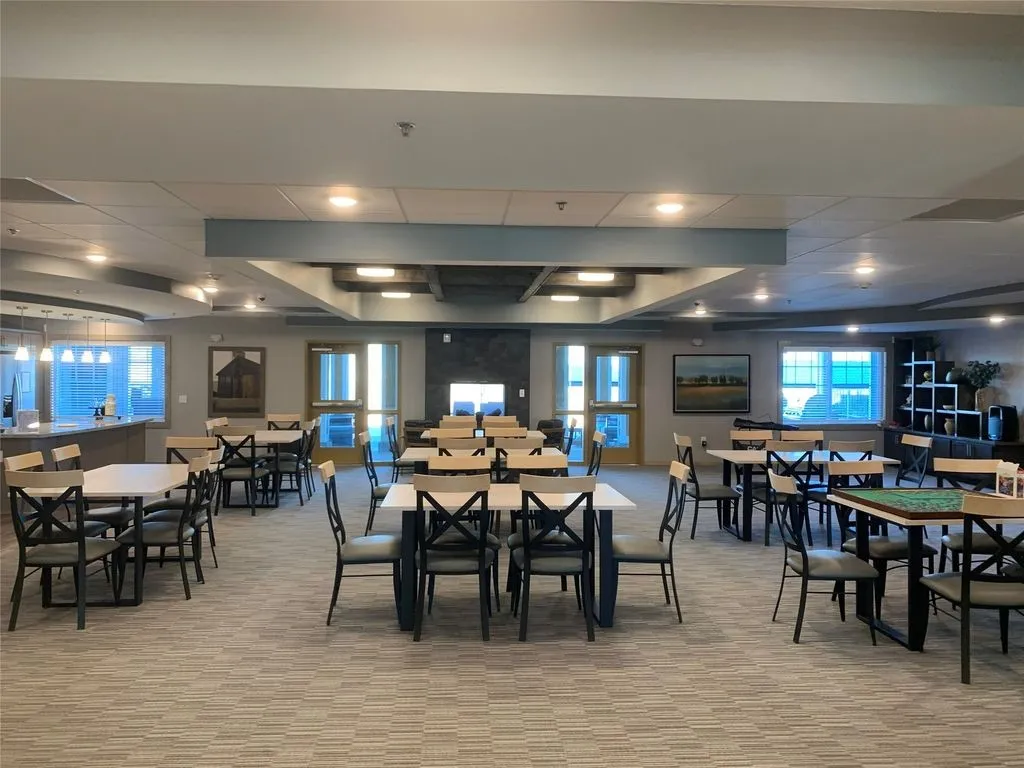 Spacious common area featuring textured carpet flooring, recessed lighting, a stone-clad fireplace, and multiple windows
