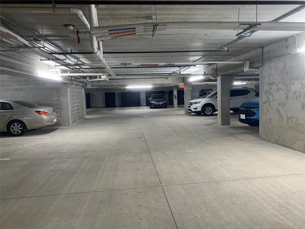 Underground parking garage featuring concrete flooring, exposed utility piping, and fluorescent lighting