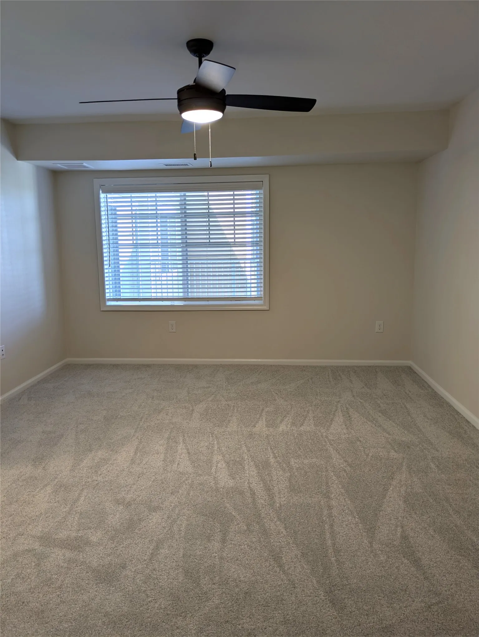 Carpeted interior space featuring a window with horizontal blinds and a ceiling fan with integrated lighting