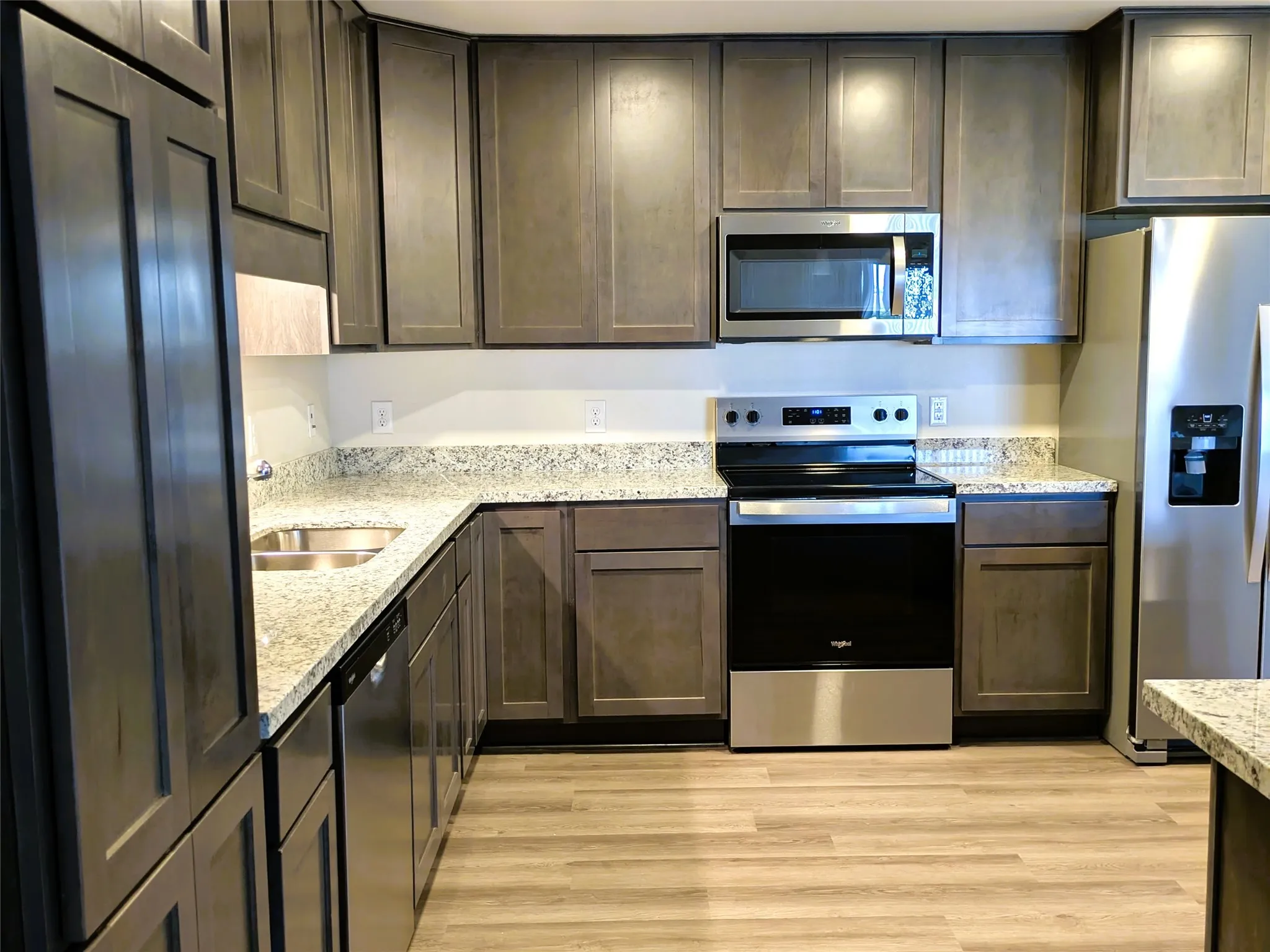 Kitchen featuring wood-finish cabinetry, granite-style countertops, stainless steel appliances, a built-in microwave, and wood-finish flooring