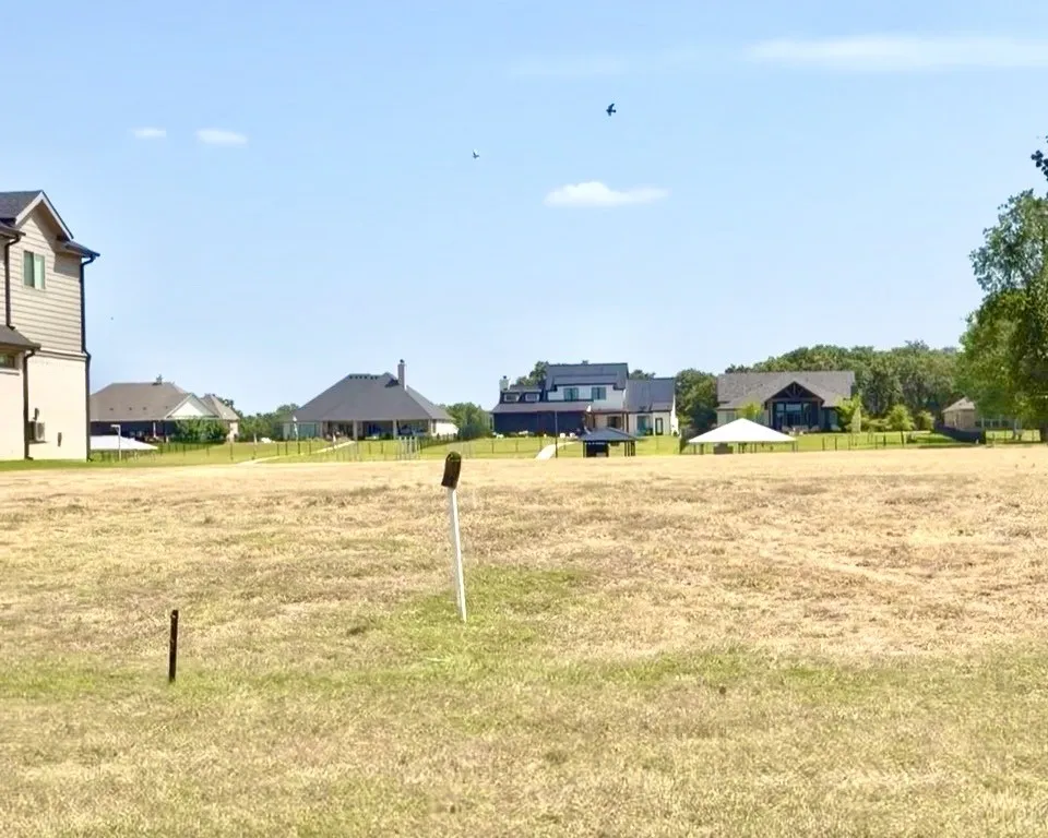 Expansive open lot featuring a clear building area, surrounding established residences, and mature trees in the background